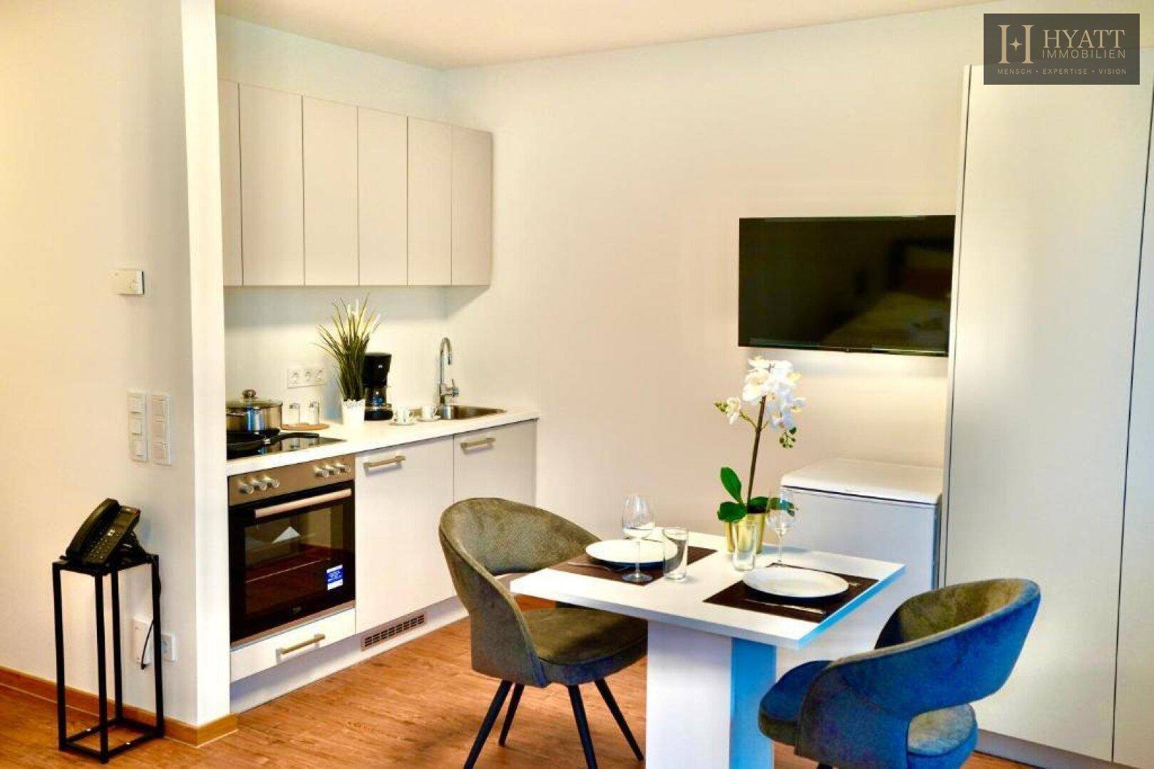 Moderne Küchenzeile mit Essbereich, integriertem Backofen und Wandfernseher in einem Studio.