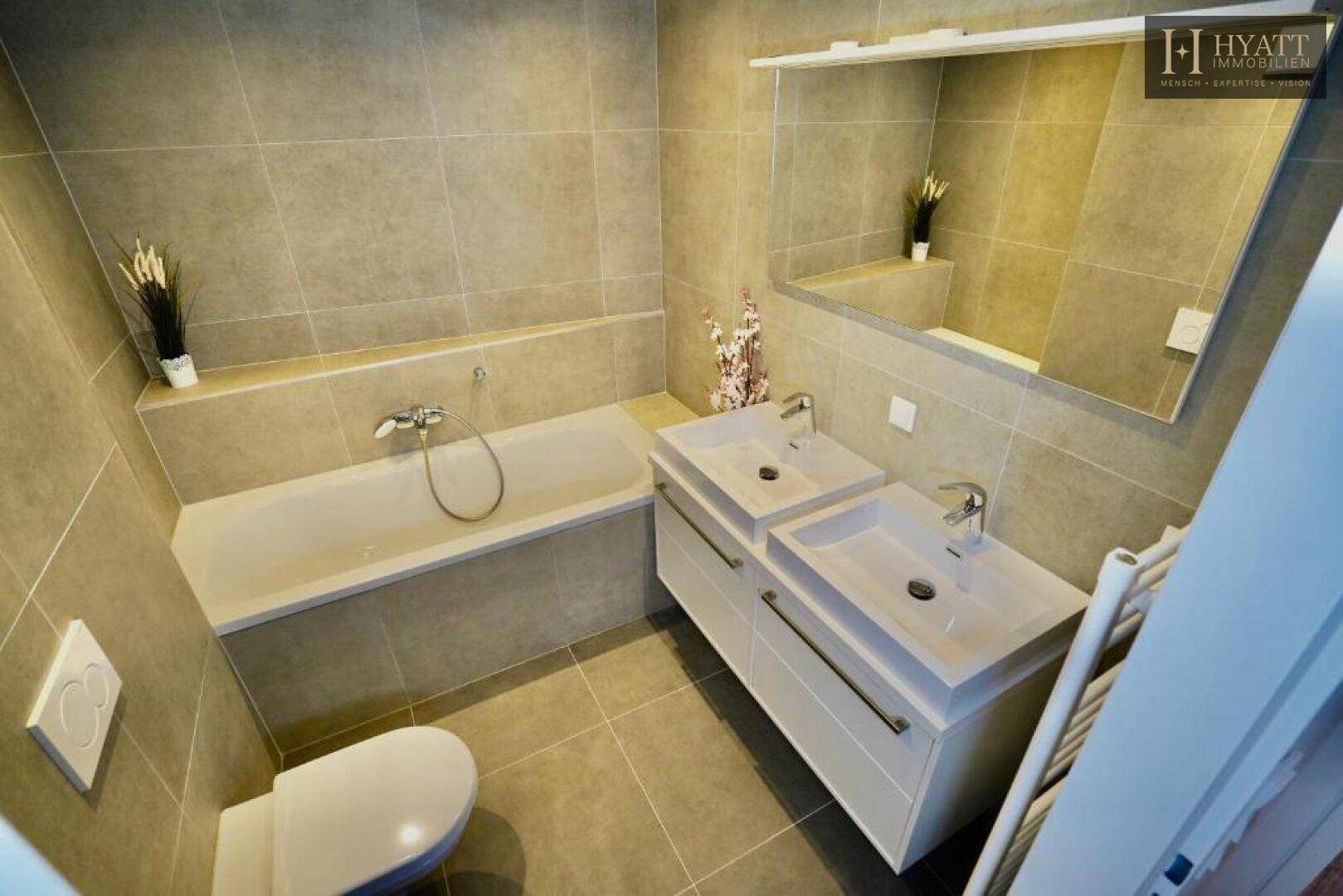 Modernes Badezimmer mit Badewanne, Doppelwaschbecken und hellen Fliesen.