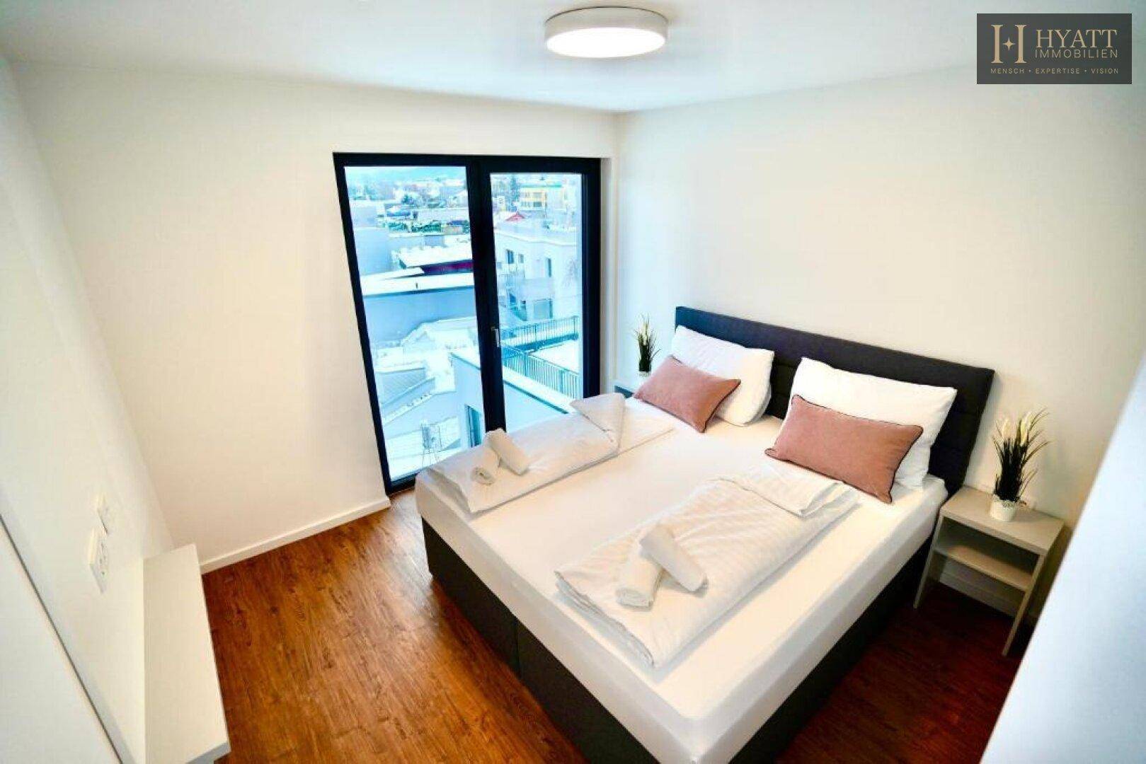 Modernes Schlafzimmer mit Doppelbett, Holzboden und großem Fenster mit Blick auf die Umgebung.
