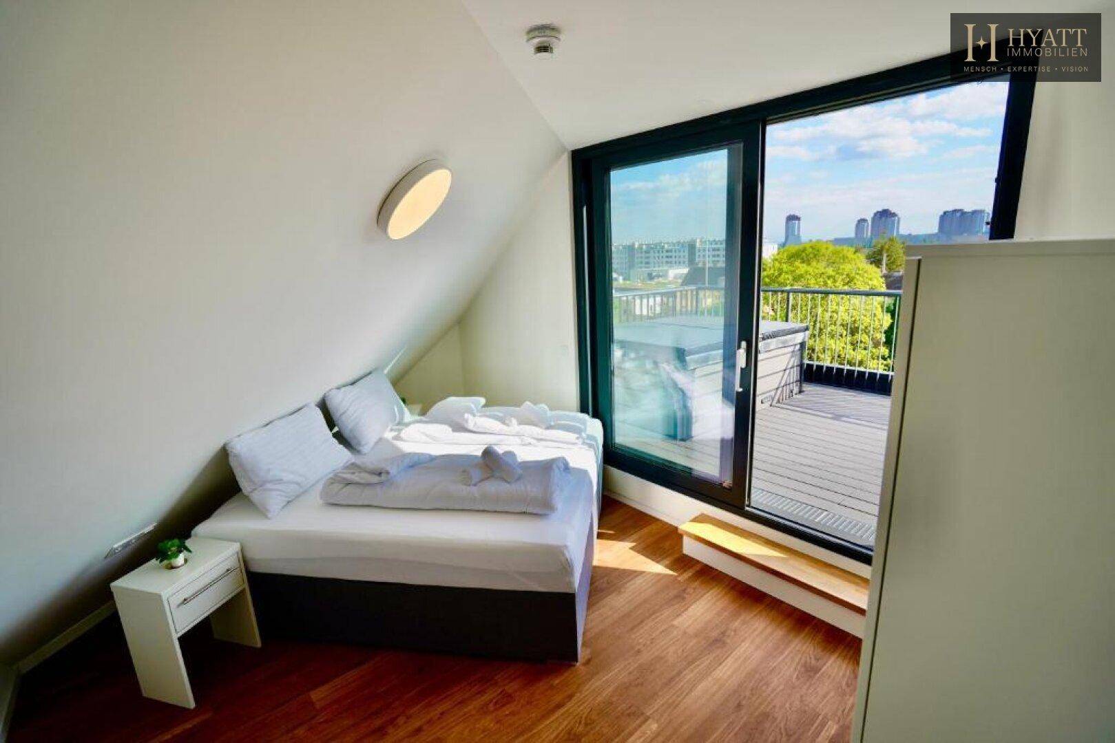 Helles Schlafzimmer mit Holzboden und direktem Zugang zu einer großen Dachterrasse.