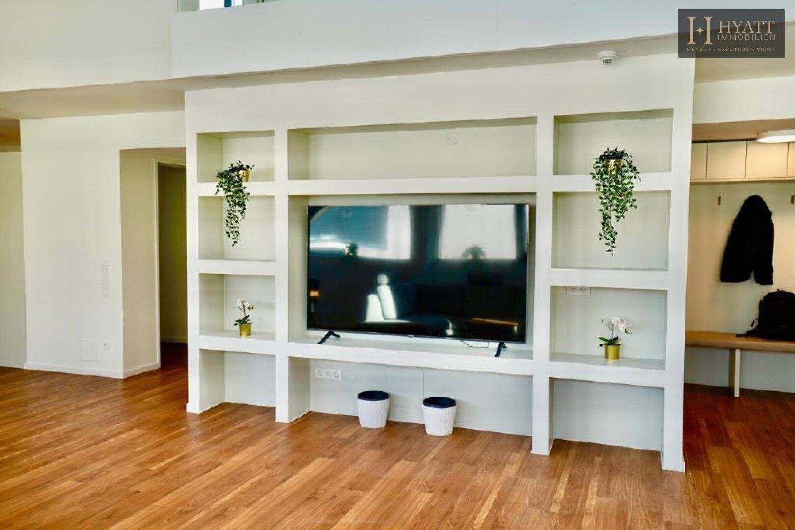 Moderner Wohnbereich mit integriertem TV-Möbel, Holzboden und Garderobe im Hintergrund.