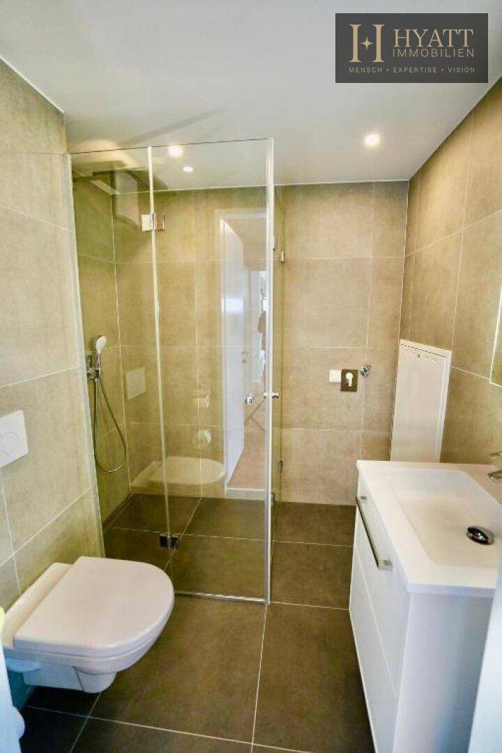 Modernes Badezimmer mit grauen Fliesen, Einzelwaschbecken und geräumiger begehbarer Dusche.