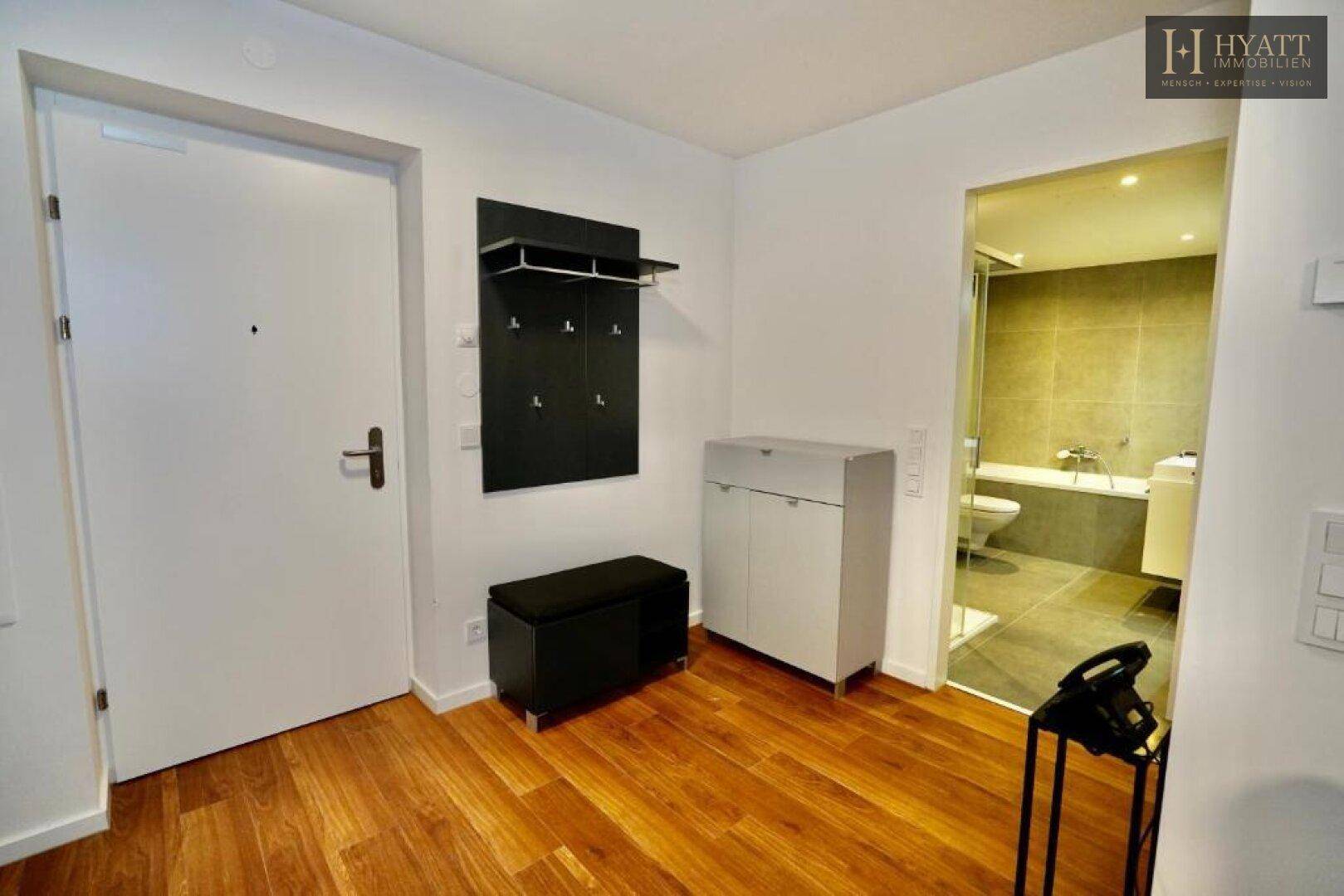 Eingangsbereich mit Garderobe und Schuhschrank, angrenzend an ein modernes Badezimmer.