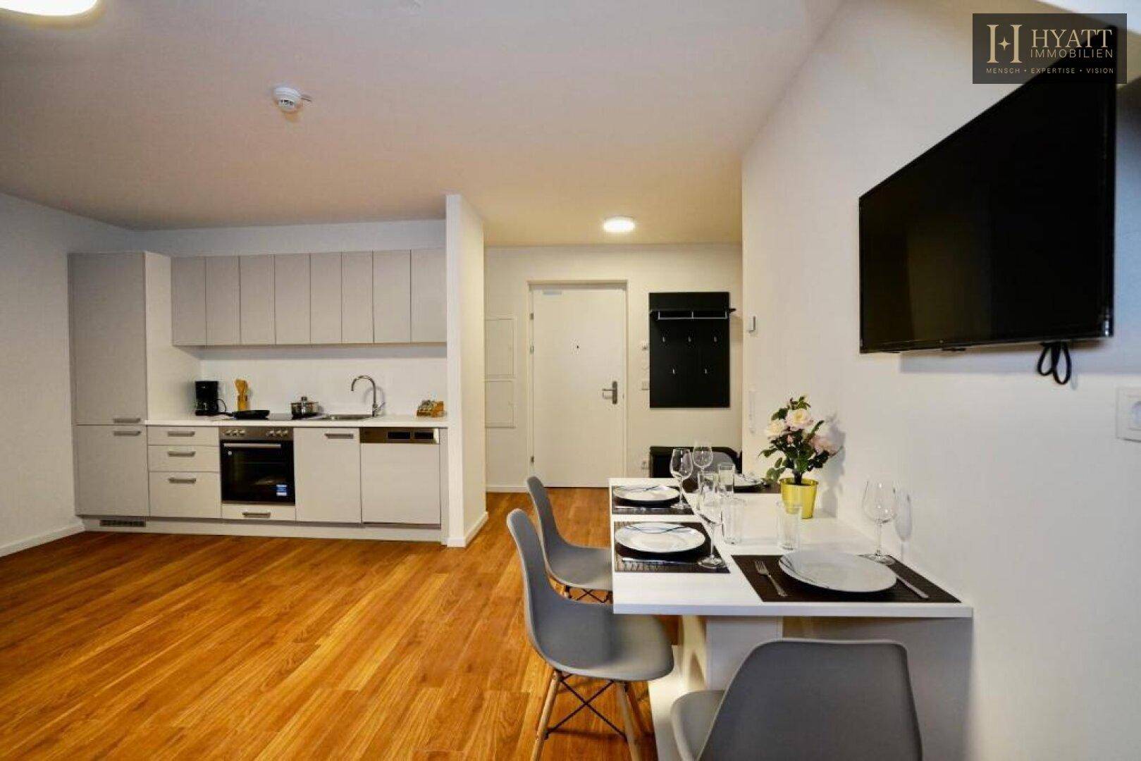Essbereich mit Wandfernseher und integrierter Küchenzeile in modernem Design.