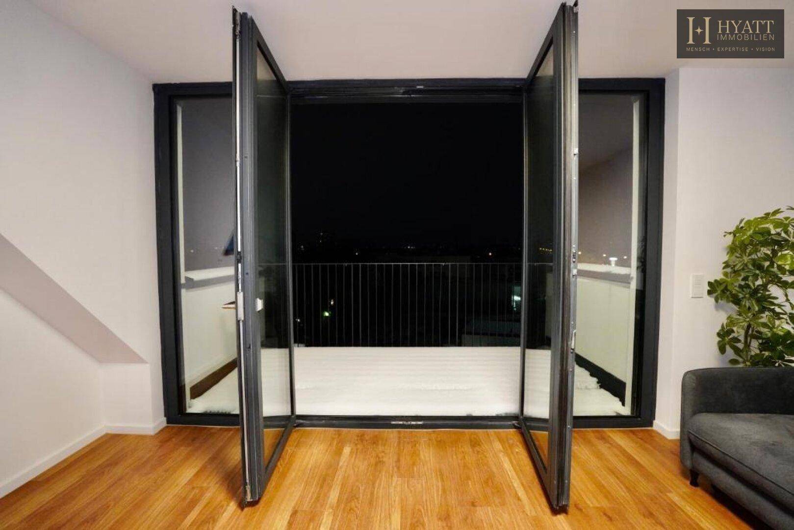 Offene Glastüren führen zu einem schneebedeckten Balkon mit Blick in die Nacht.