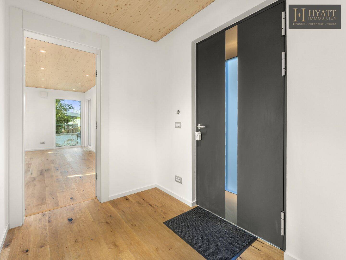Heller Eingangsbereich mit Holzboden und moderner Haustür, die in den Wohnbereich führt.