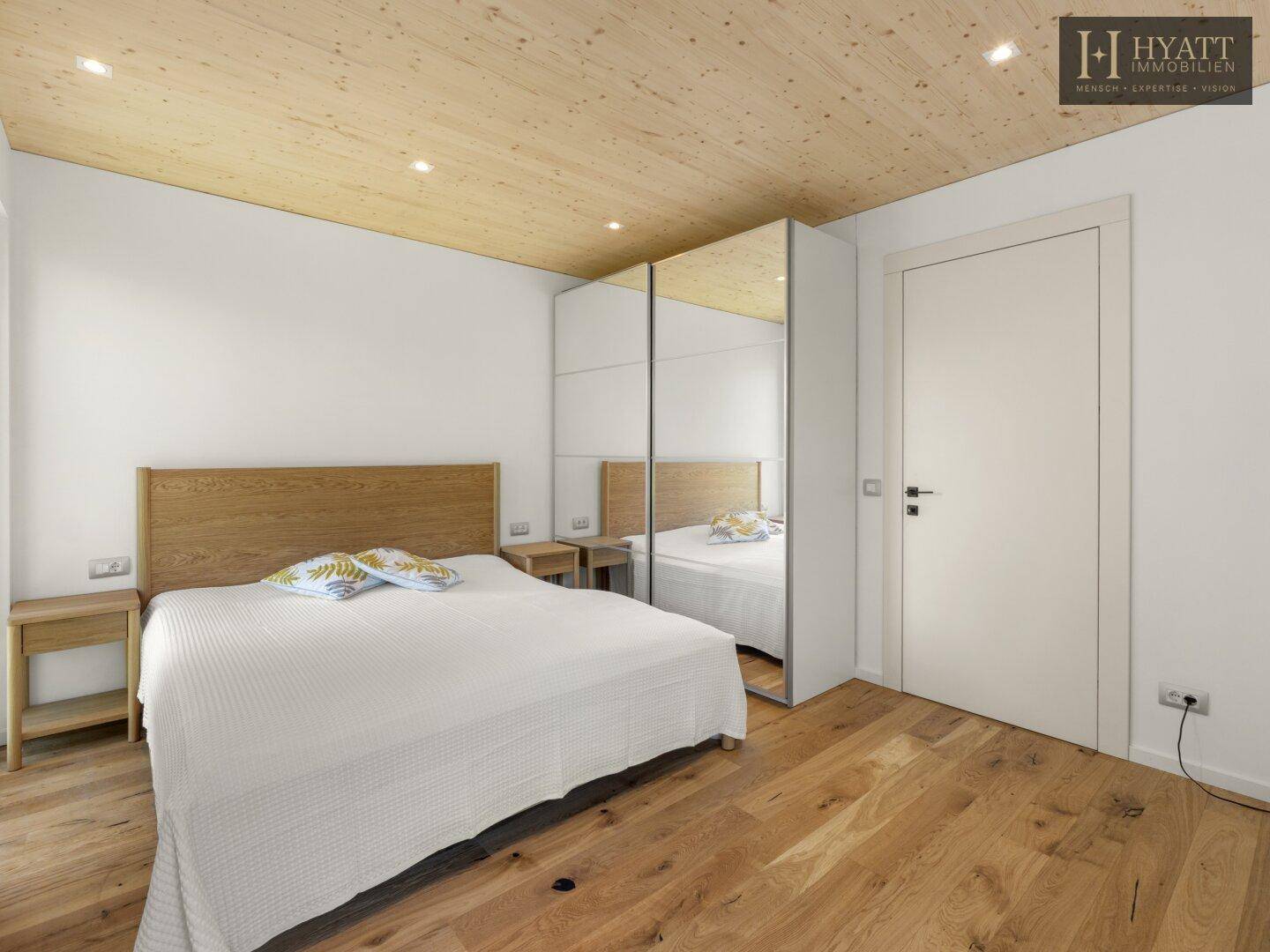 Gemütliches Schlafzimmer mit Holzboden, großem Bett und Spiegelschränken für viel Stauraum.