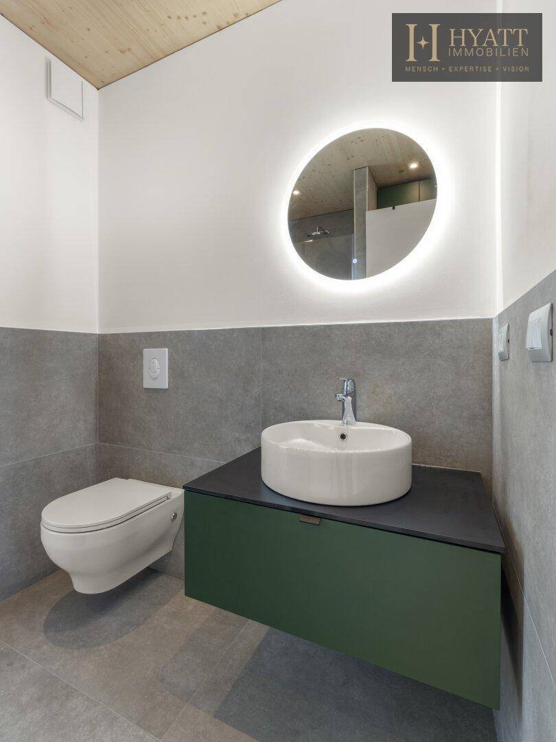 Modernes WC mit wandhängender Toilette, Aufsatzwaschbecken und beleuchtetem Spiegel.