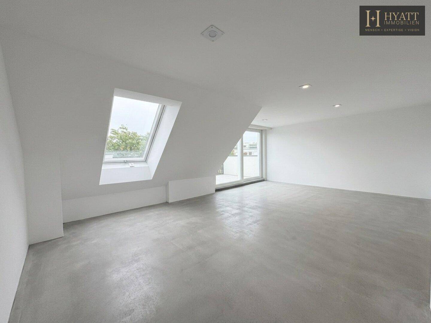 Leerer Raum im Dachgeschoss mit Betonboden, Dachschräge und Zugang zu einem Außenbereich.