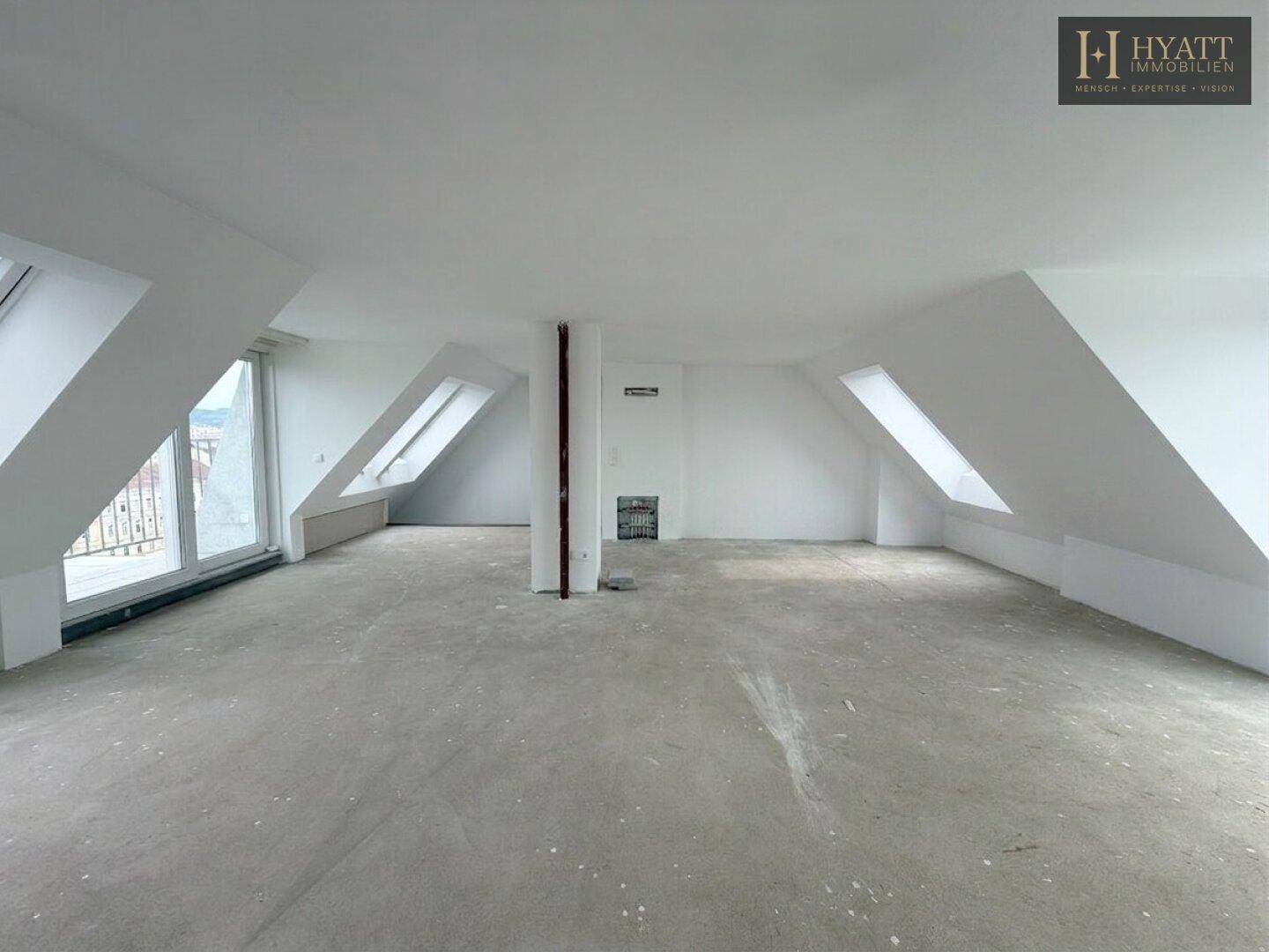 Geräumiger, unmöblierter Dachgeschossraum mit Betonboden, Dachschrägen und vielen Fenstern.