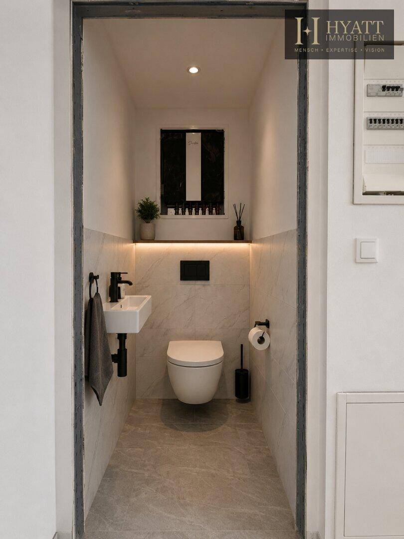 Modernes Gäste-WC mit wandhängender Toilette, kleinem Waschbecken und stilvollen Fliesen.
