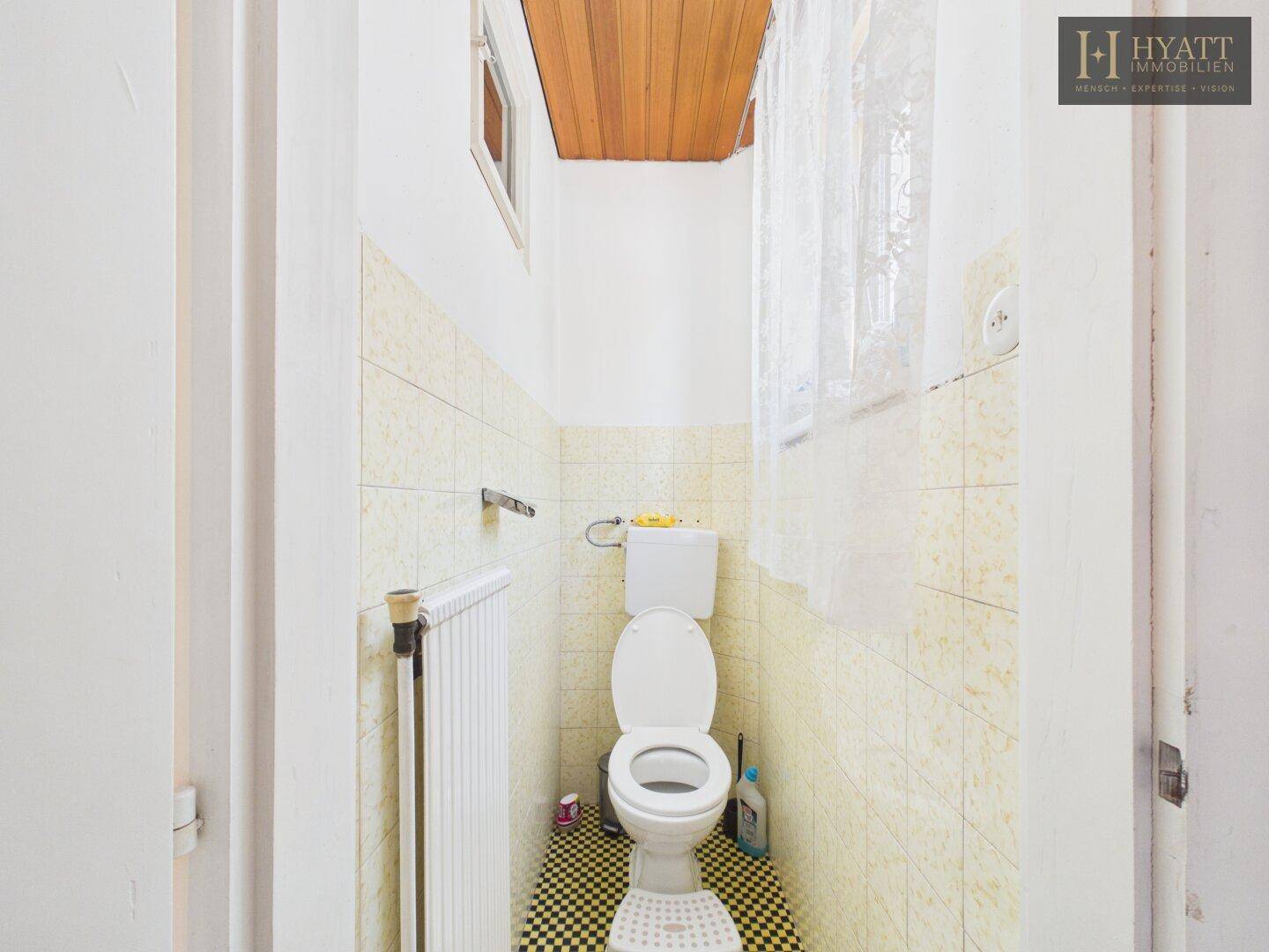 Kleines Gäste-WC mit gelben Fliesen, Standard-WC und Fenster.