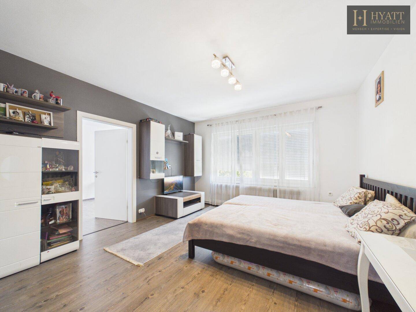 Helles Schlafzimmer mit Holzboden, weißer Wand und einfacher Möblierung.