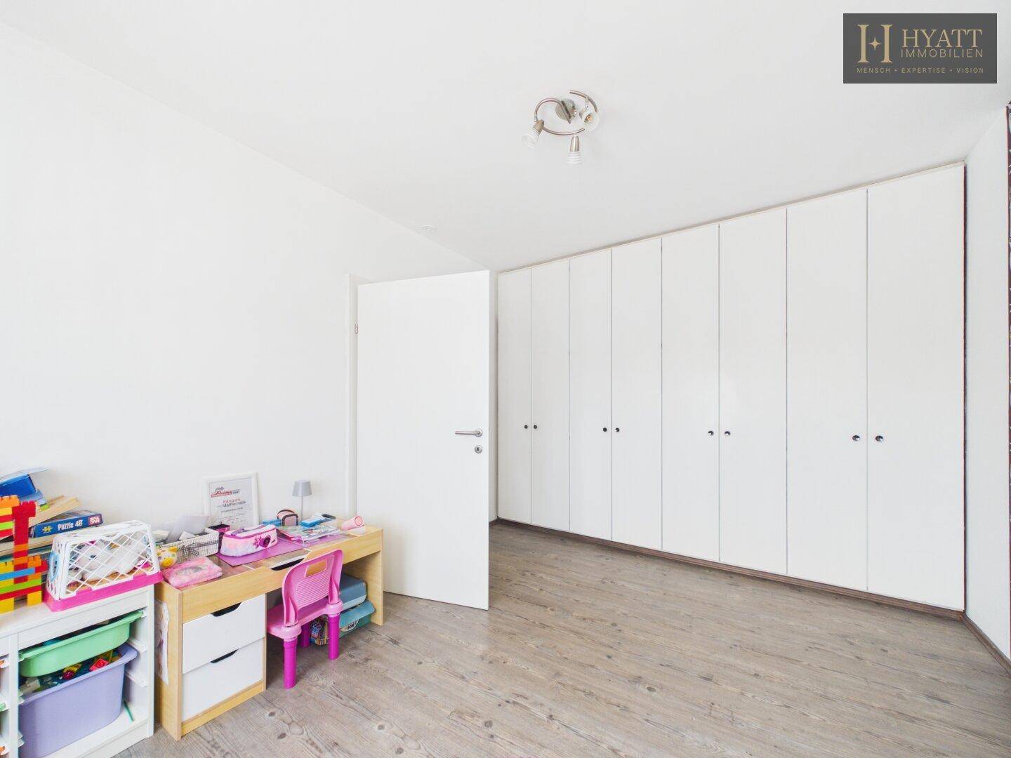 Kinderzimmer mit langen weißen Einbauschränken und hellem Laminatboden.