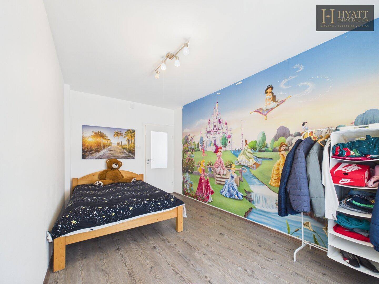 Helles Kinderzimmer mit Prinzessinnen-Wandbild, Holzbett und Kleiderständer.