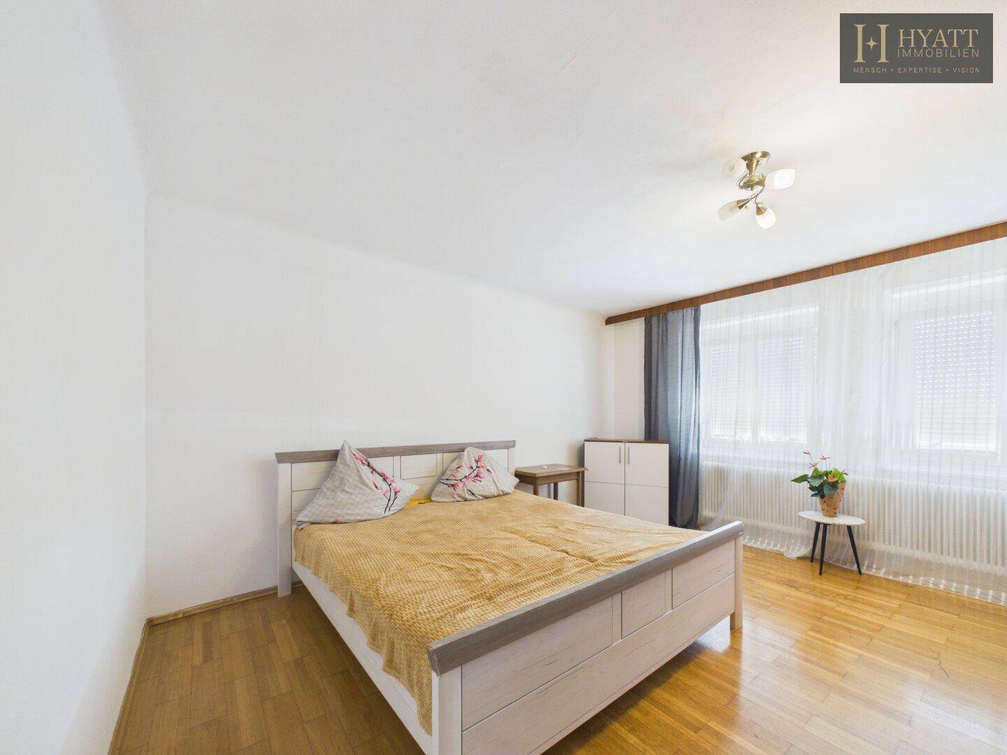 Geräumiges Schlafzimmer mit Holzboden, hellem Bett und großen Fenstern.