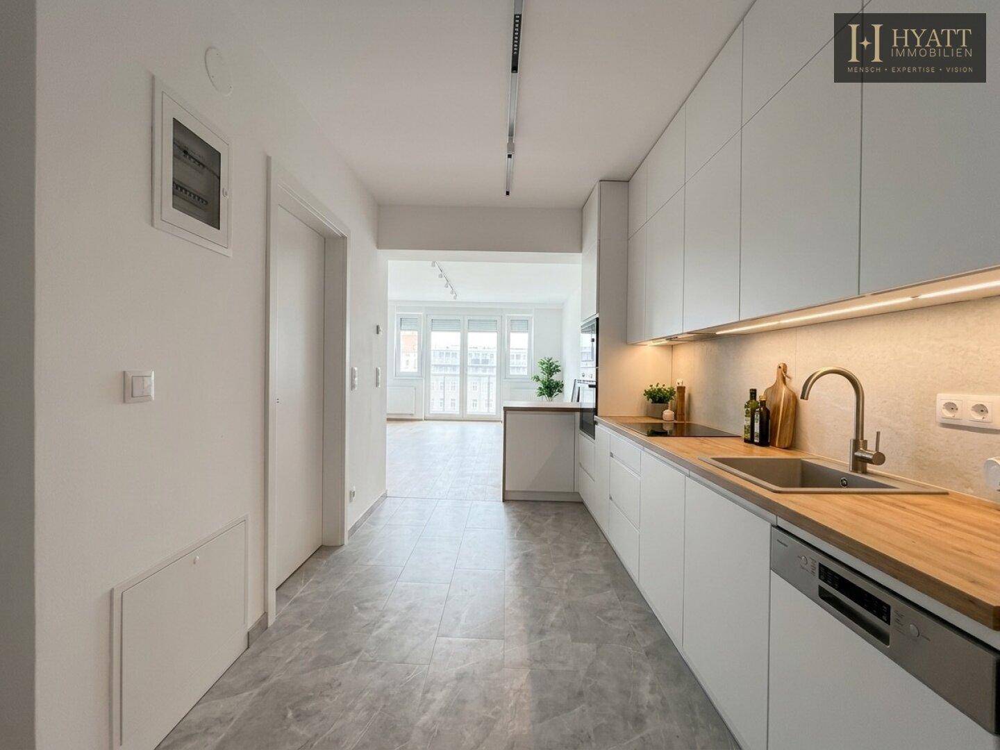 Moderne, helle Küche mit weißen Schränken, Holz-Arbeitsplatte und Fliesenboden, offen zum Wohnbereich.
