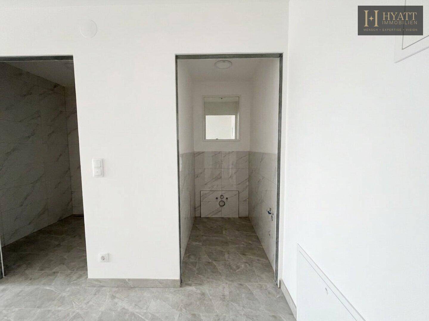 Kleines Gäste-WC im Rohbau mit Fliesen an den Wänden und einem kleinen Spiegel.