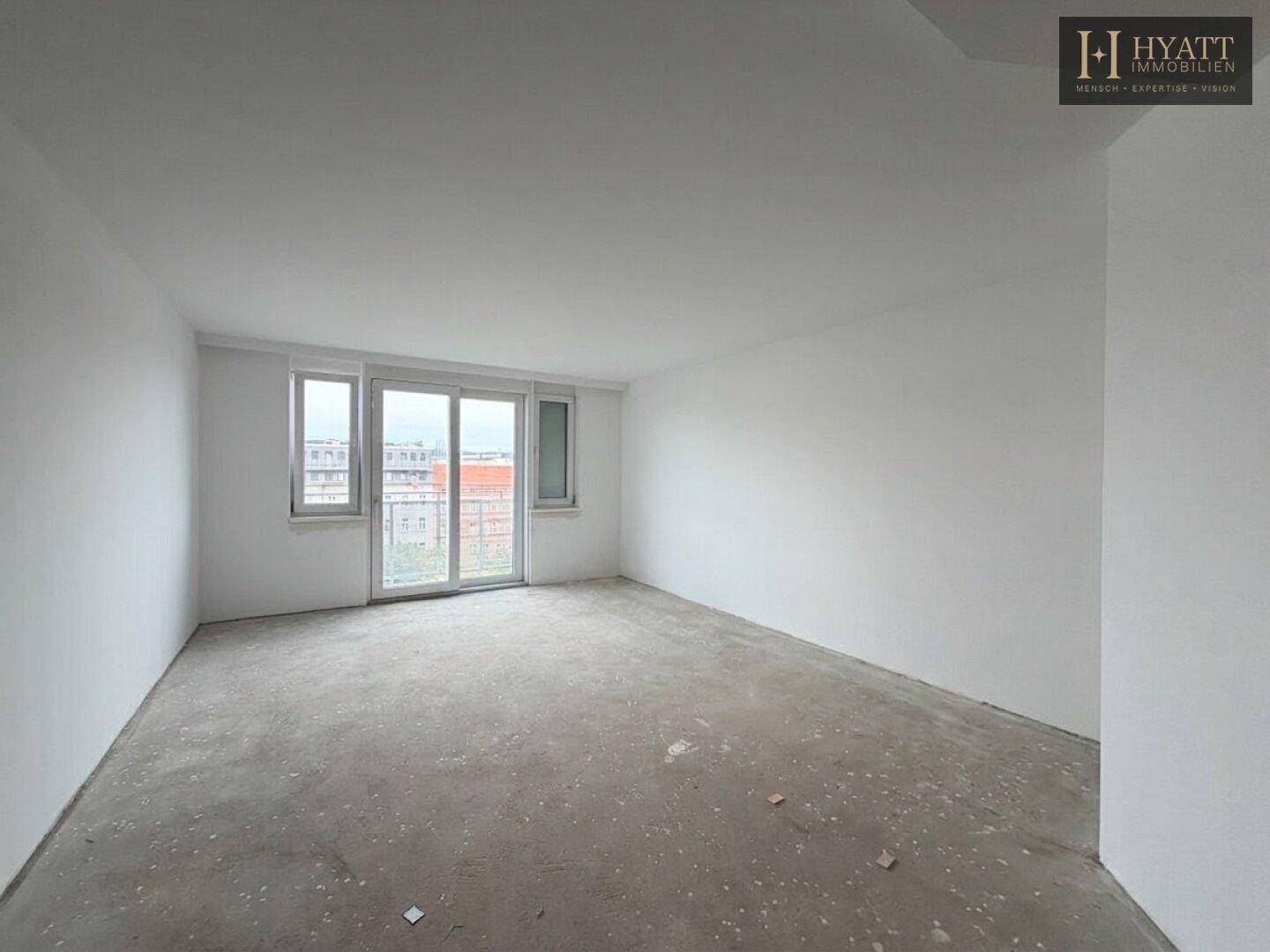 Unmöblierter Wohnraum im Rohbau mit großem Fenster und Zugang zu einem möglichen Balkon.