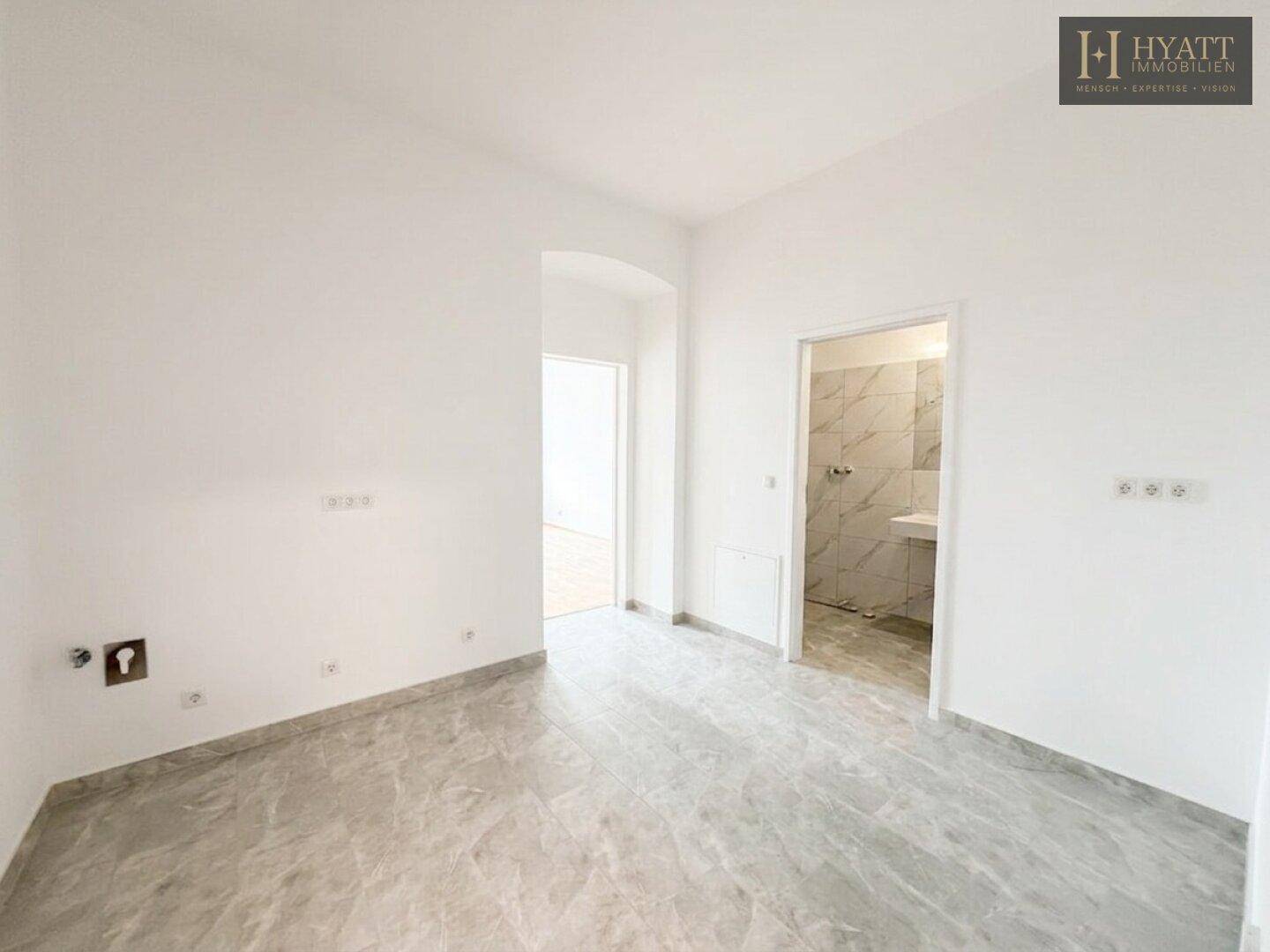 Heller Raum mit Fliesenboden und vorbereiteten Anschlüssen, mit Zugang zu einem gefliesten Badezimmer.
