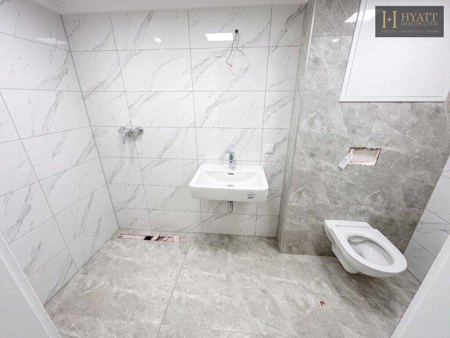 Modernes Badezimmer mit grauen und weißen Fliesen, wandhängendem WC und Waschbecken.