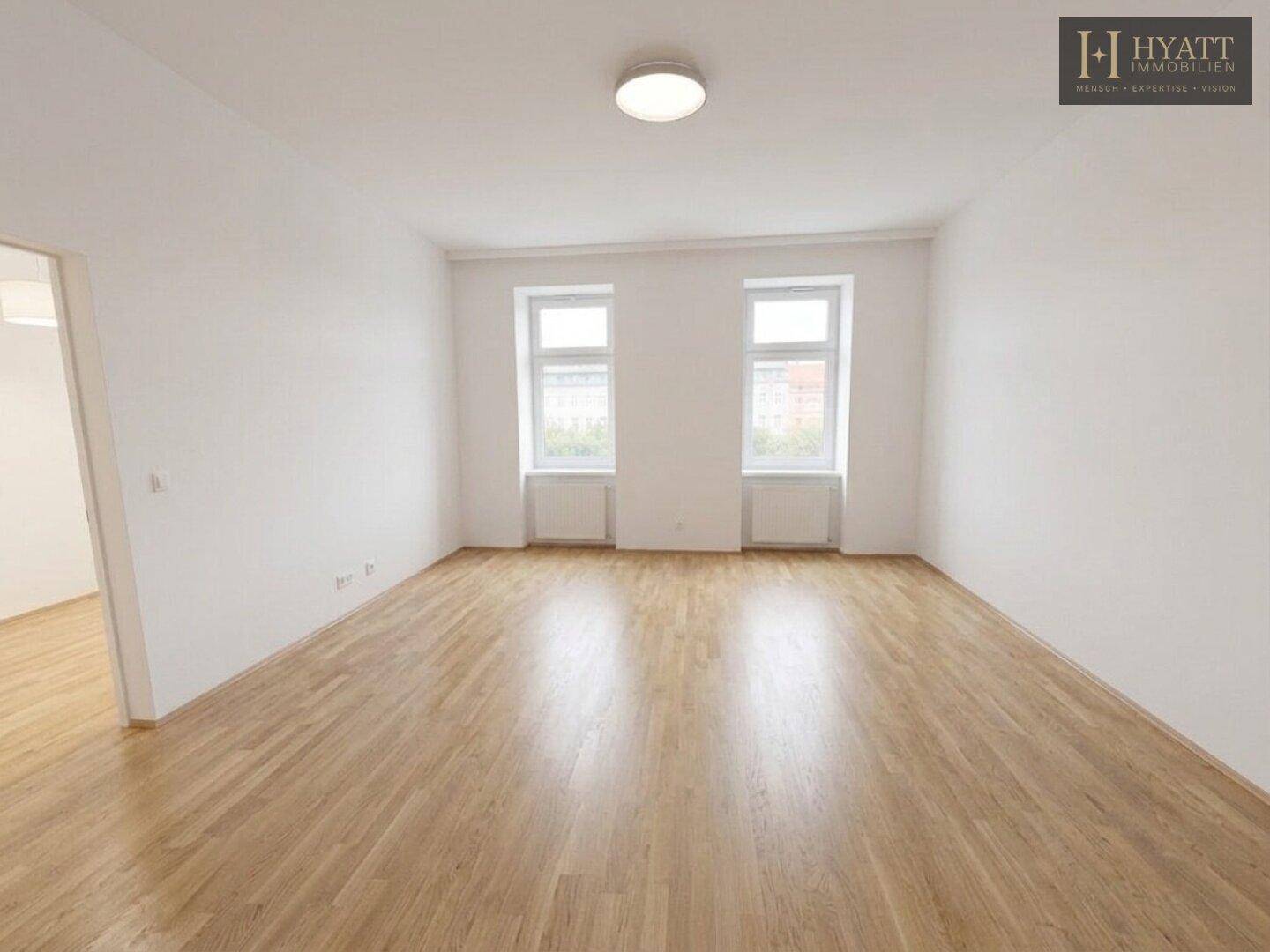 Helles, leeres Zimmer mit Parkettboden und zwei großen Fenstern, bereit zur individuellen Gestaltung.