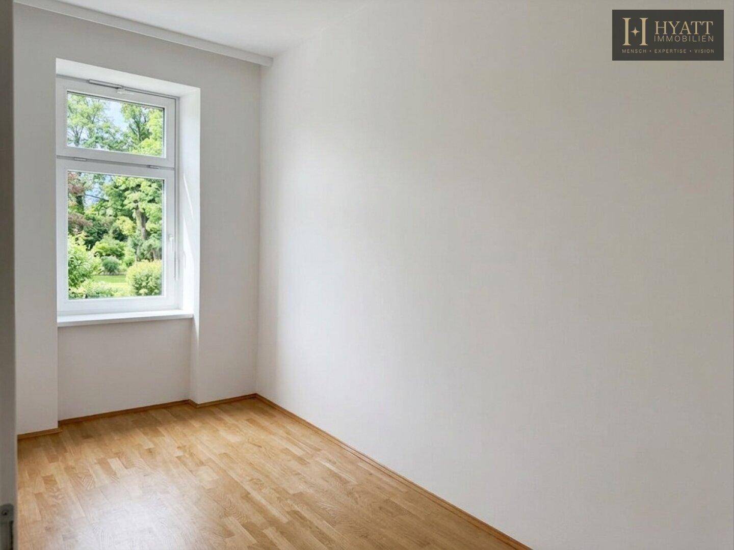 Helles, unmöbliertes Zimmer mit Holzboden und Fenster mit Blick ins Grüne.
