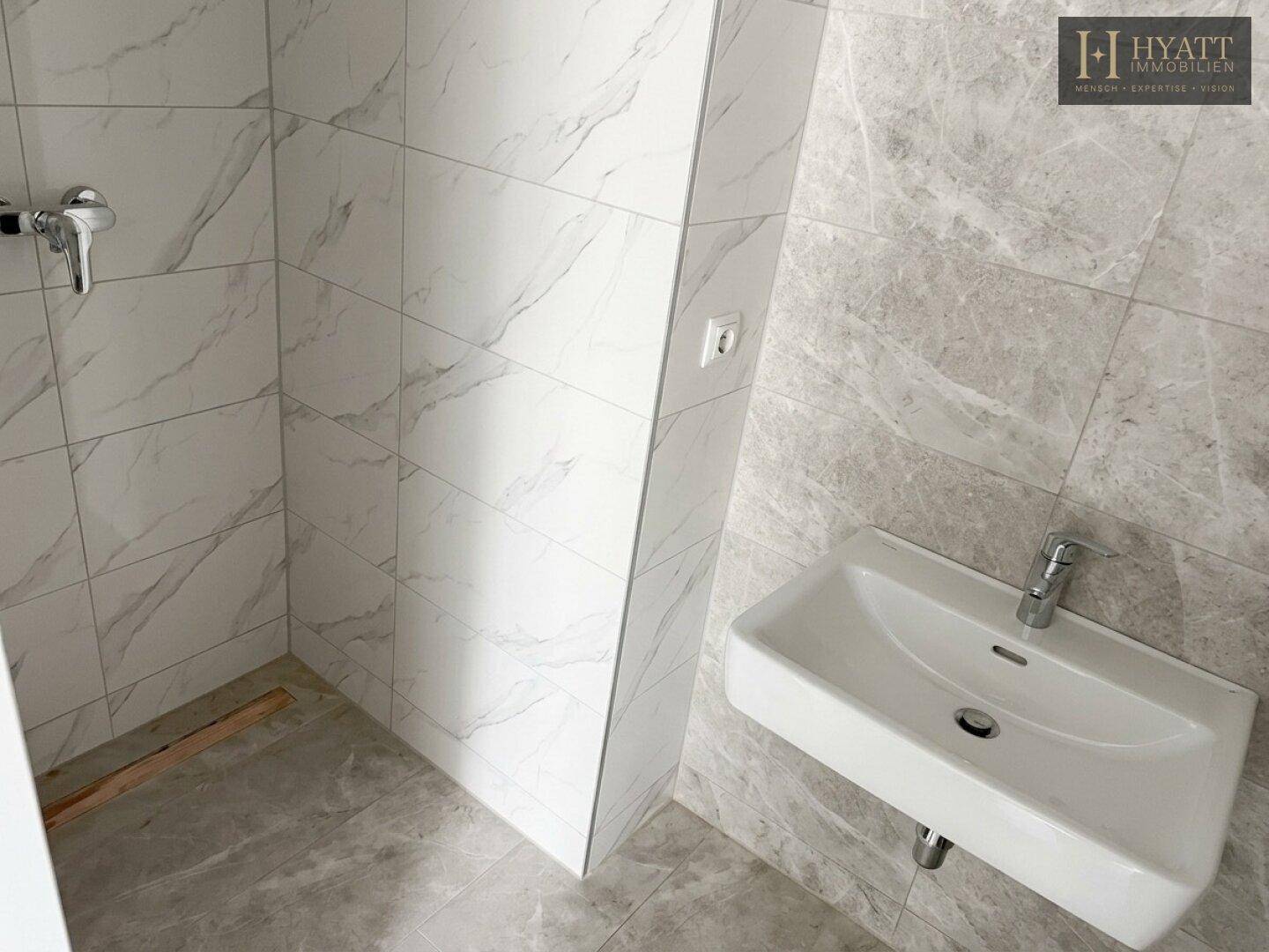 Modern gefliestes Badezimmer mit Waschbecken und vorbereitetem Duschbereich.