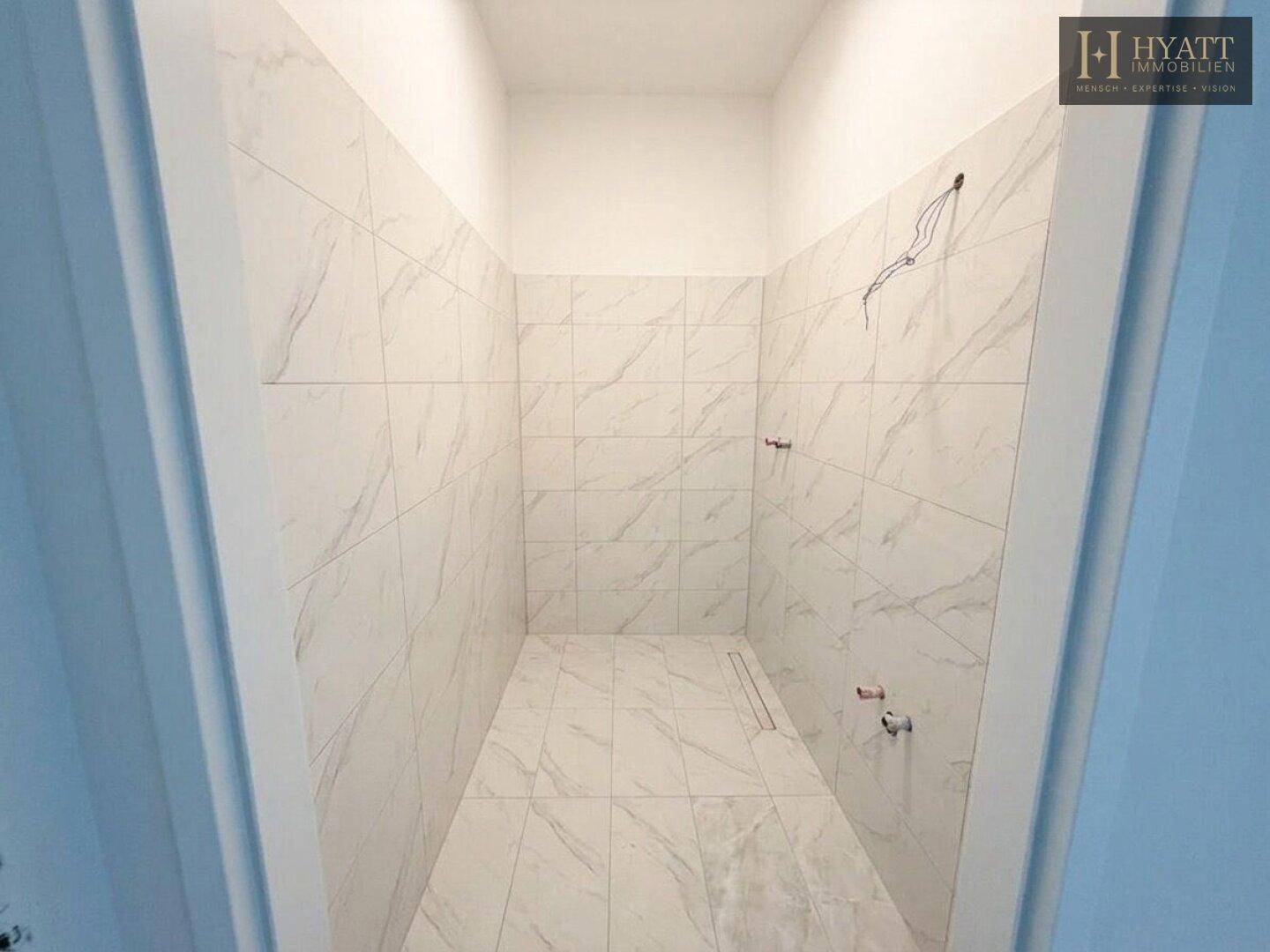 Badezimmer im Rohbau mit eleganten weißen Marmorfliesen an Wänden und Boden.