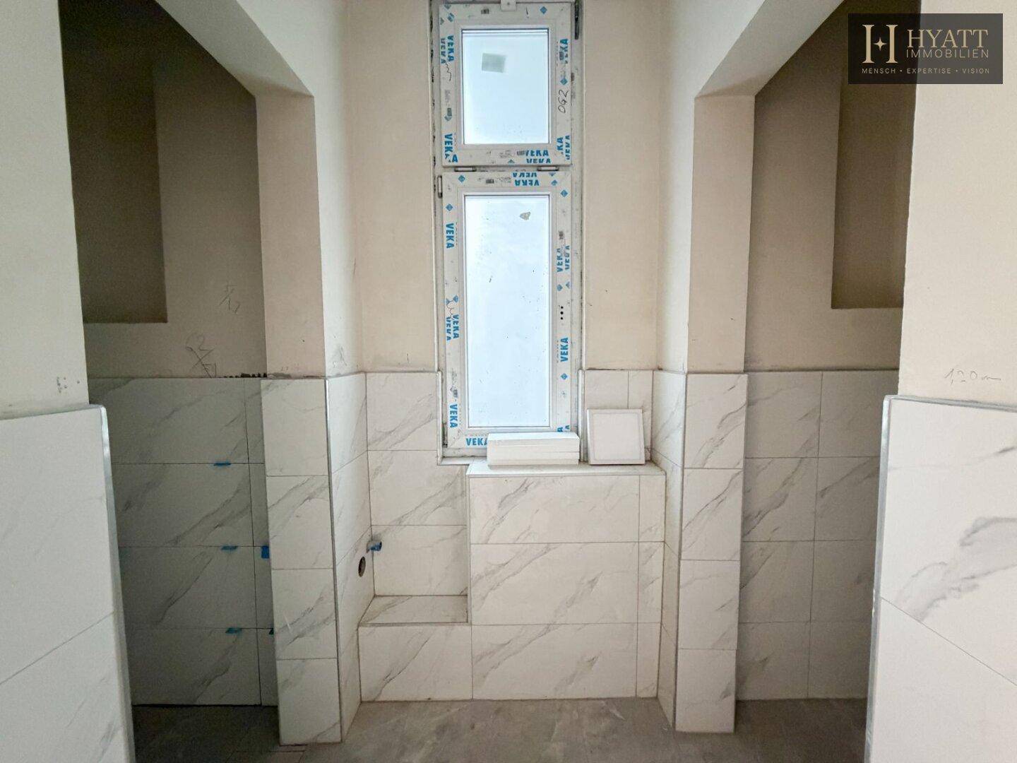 Badezimmer im Rohbau mit Fenster und vorbereiteten Anschlüssen für Waschtisch und WC.