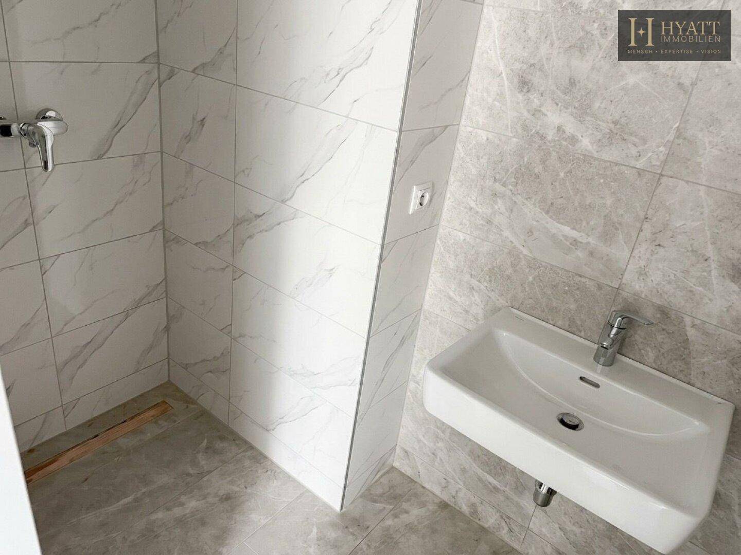 Helles Badezimmer mit modernem Waschbecken und vorbereitetem Duschbereich, komplett gefliest.