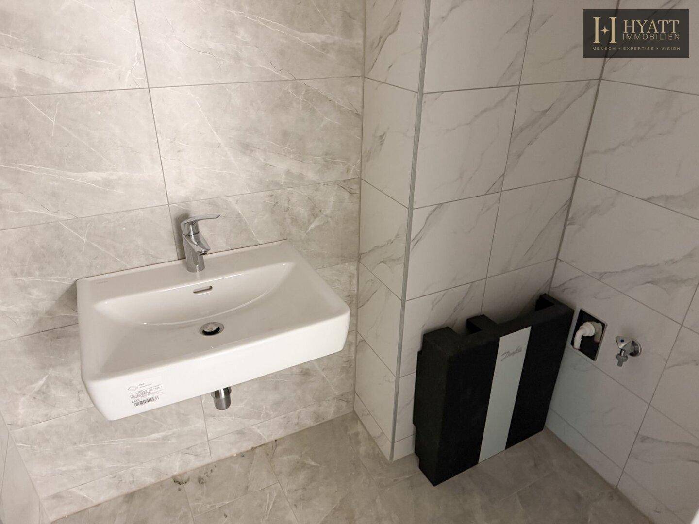 Modern gefliestes Badezimmer mit kleinem Waschbecken und Vorbereitung für weitere Installationen.