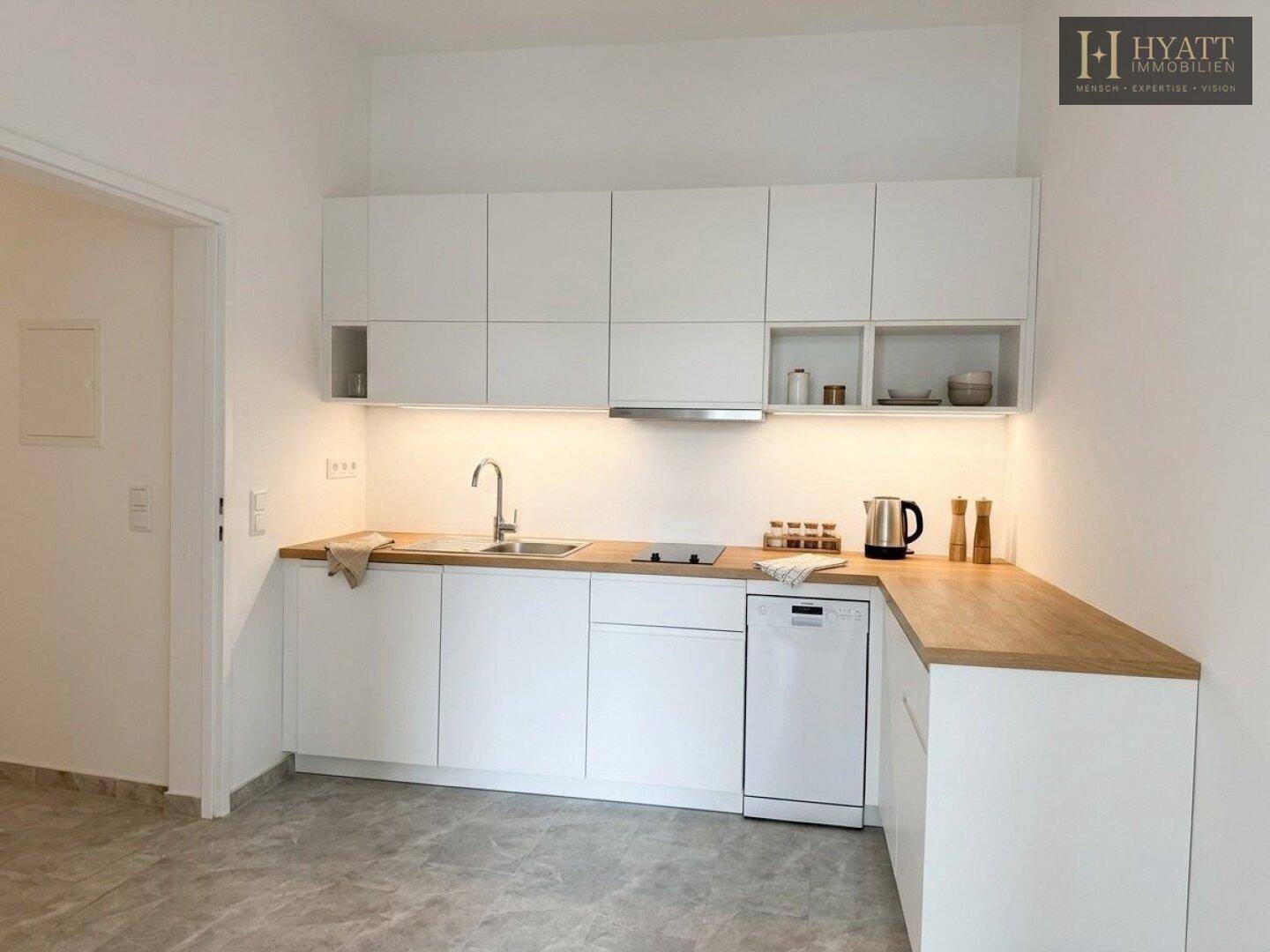 Moderne Einbauküche mit weißen Schränken, Holz-Arbeitsplatte und integriertem Geschirrspüler.