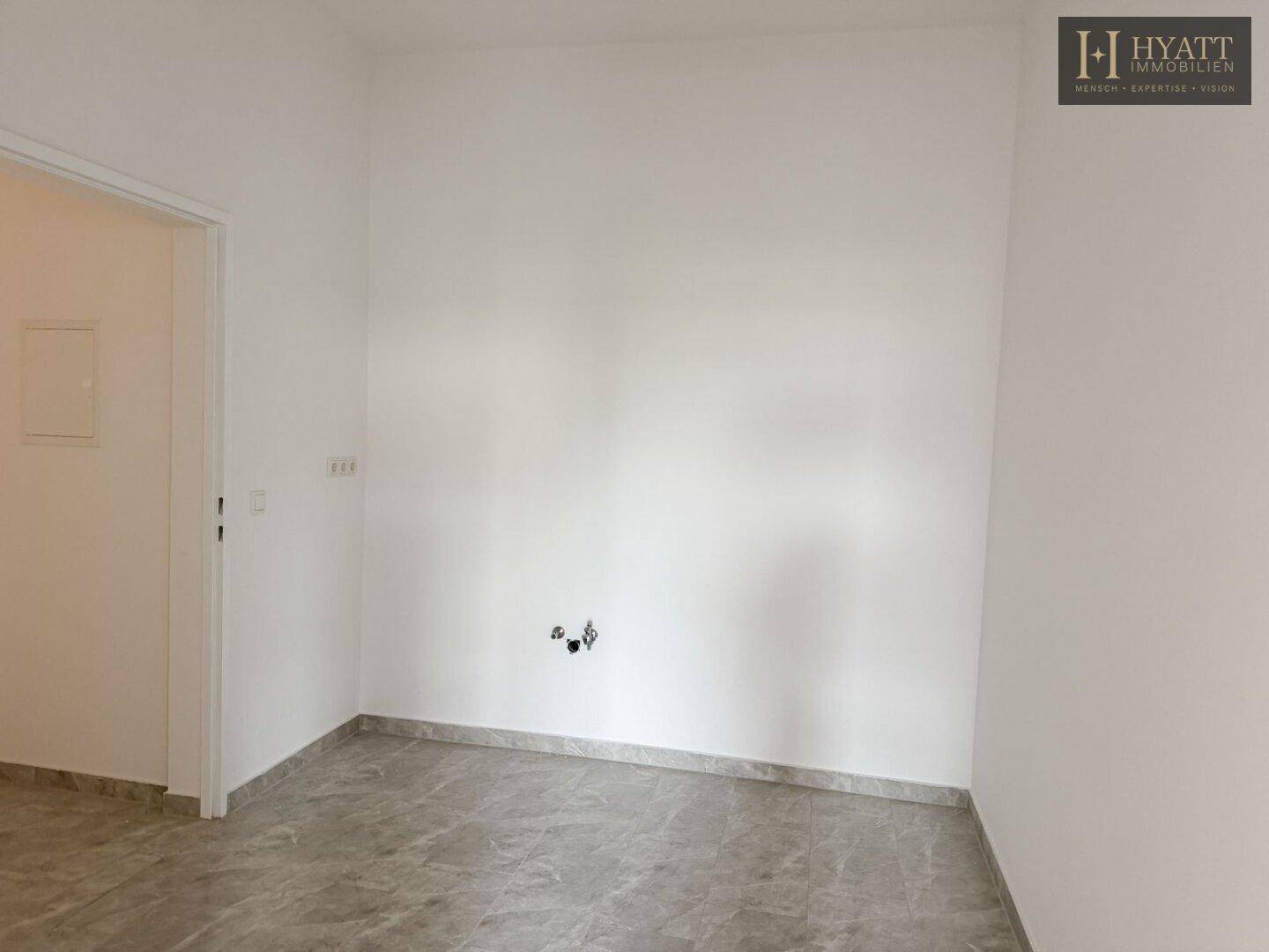 Leerer Küchenbereich mit Fliesenboden und Anschlüssen für eine zukünftige Einbauküche.