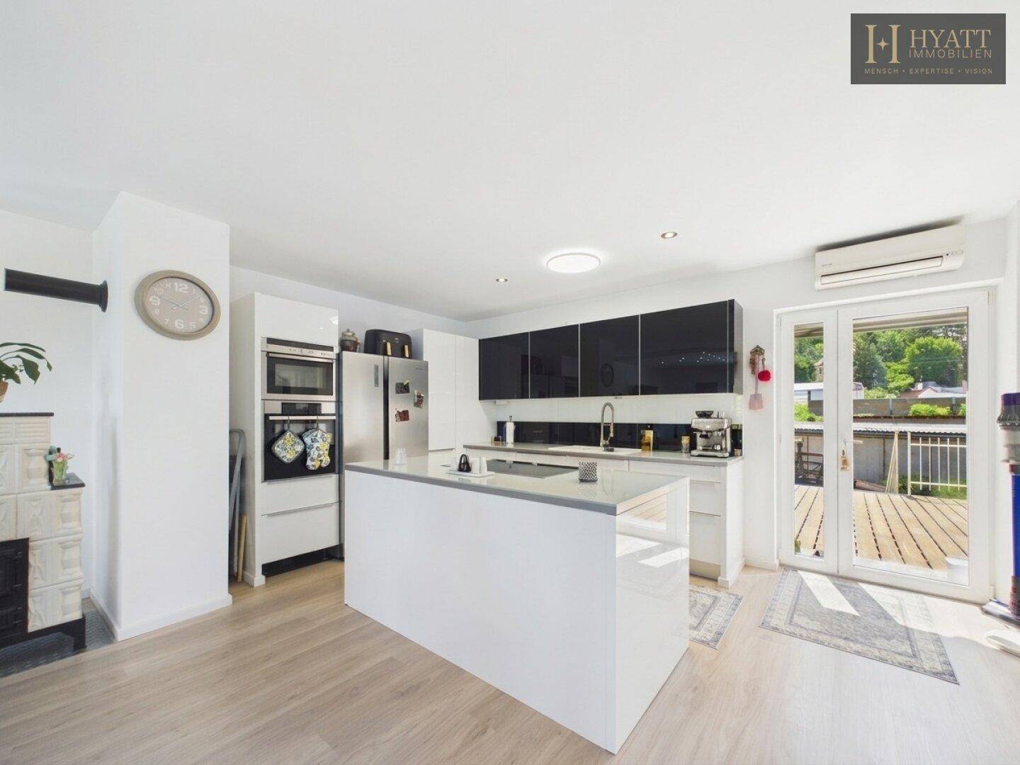 Moderne Küche mit weißer Hochglanzinsel, schwarzen Oberschränken und Zugang zur Terrasse.