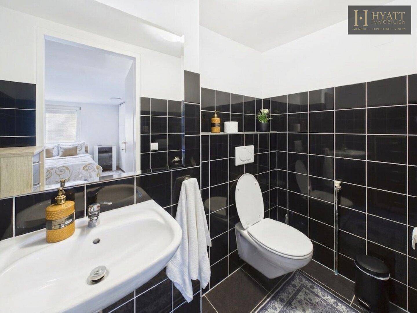 Modernes WC mit schwarzen Fliesen, wandhängendem WC und Einzelwaschbecken.