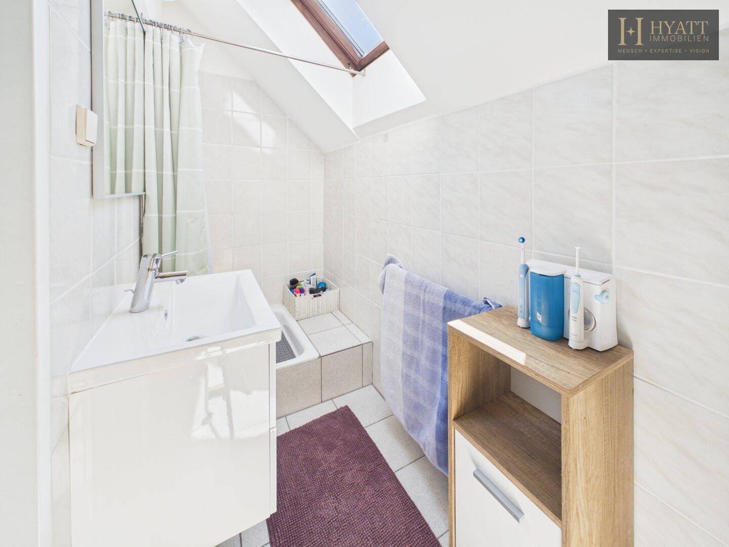 Helles Badezimmer mit Badewanne, Dachfenster und weißen Fliesen.