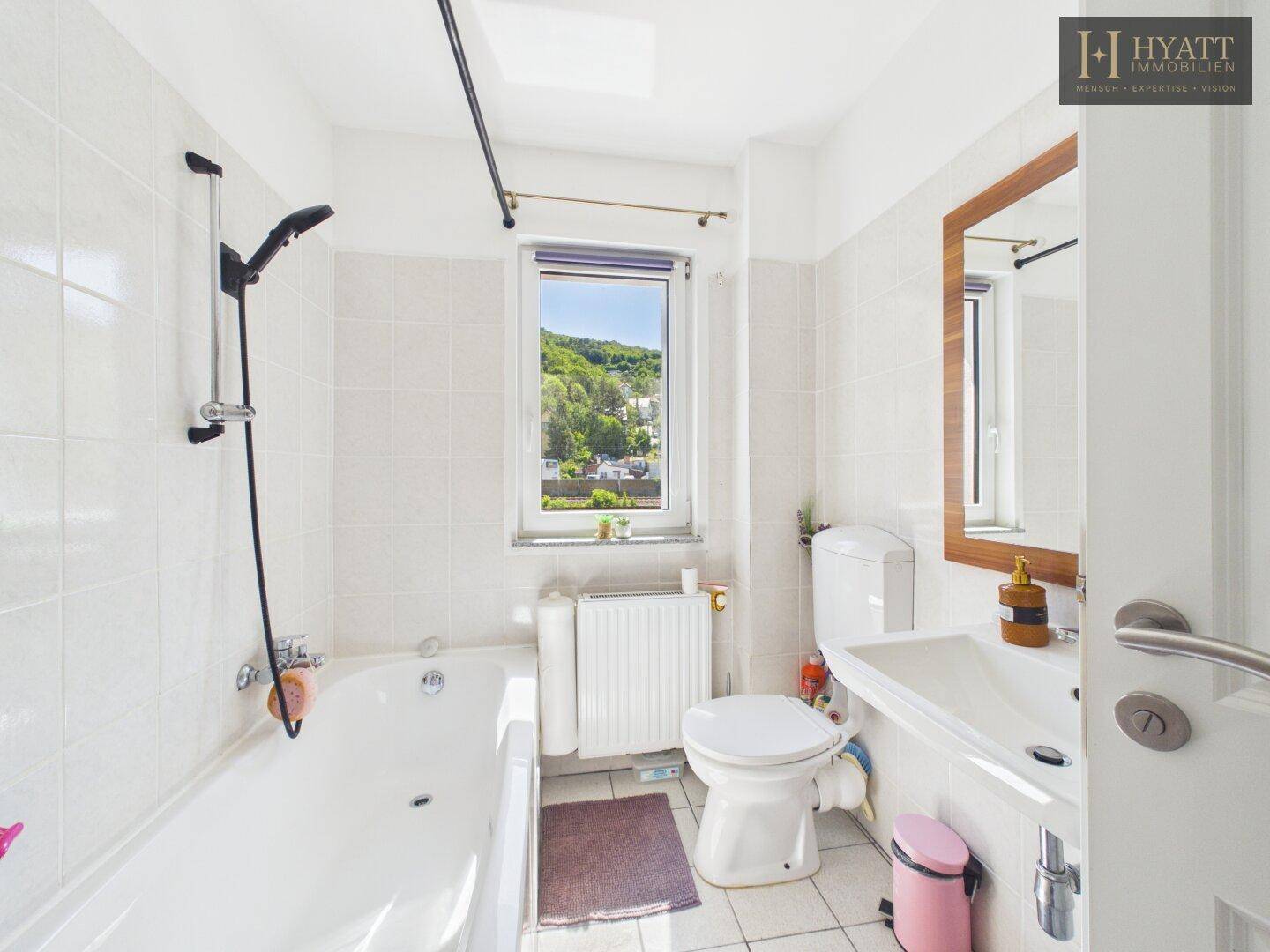 Helles Badezimmer mit Badewanne, Dusche, Fenster und Blick ins Grüne.