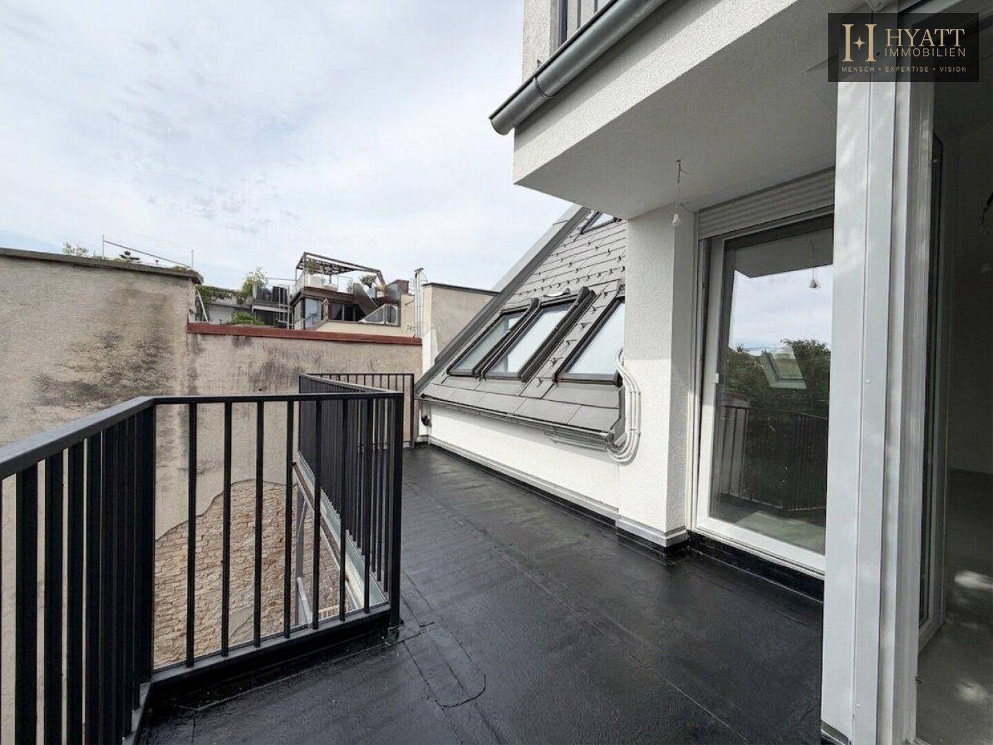 Unmöblierte Dachterrasse mit schwarzem Geländer und Blick auf die Umgebung.
