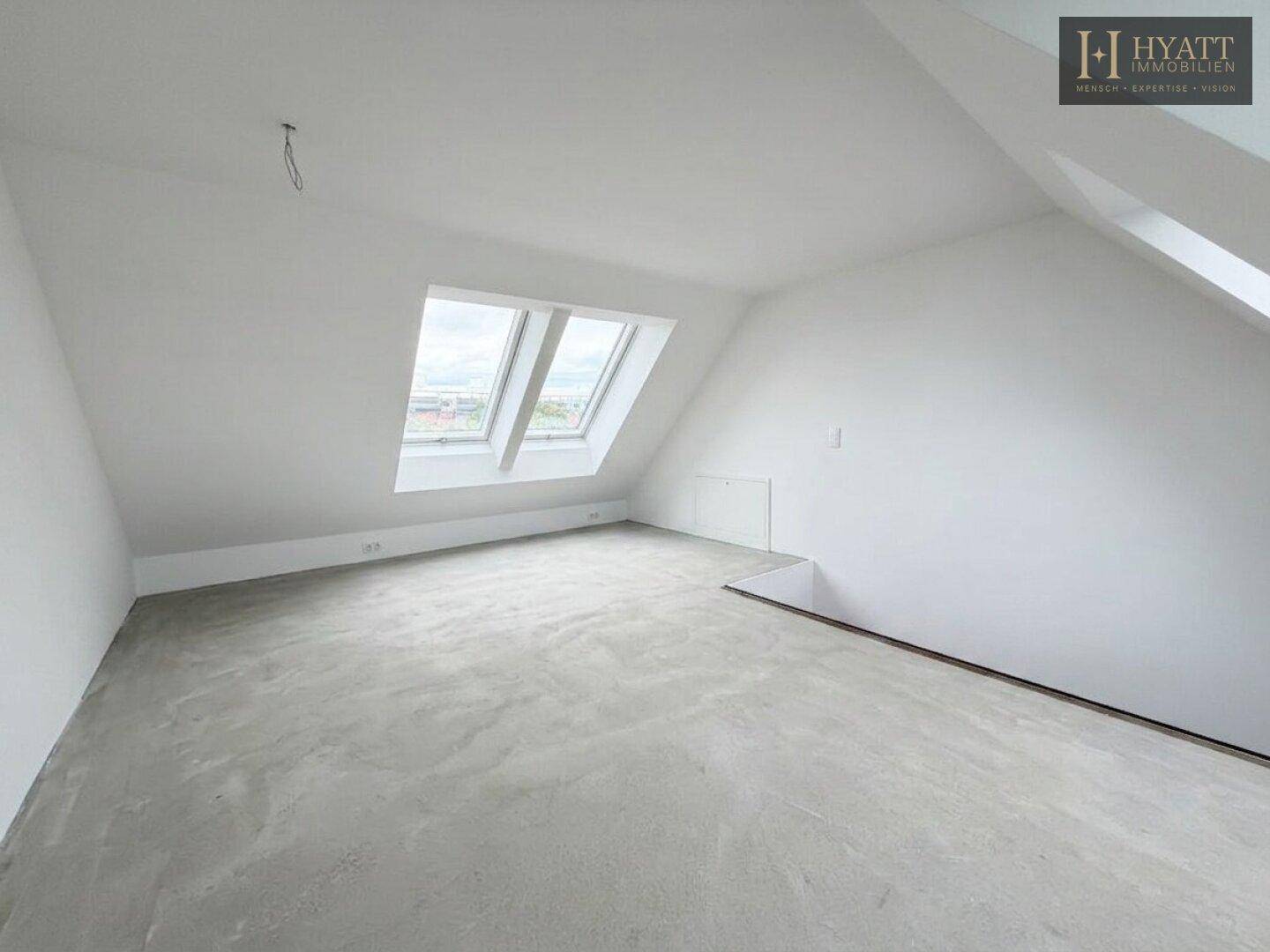 Geräumiger, unmöblierter Raum im Rohbau mit zwei Dachfenstern und Dachschrägen.