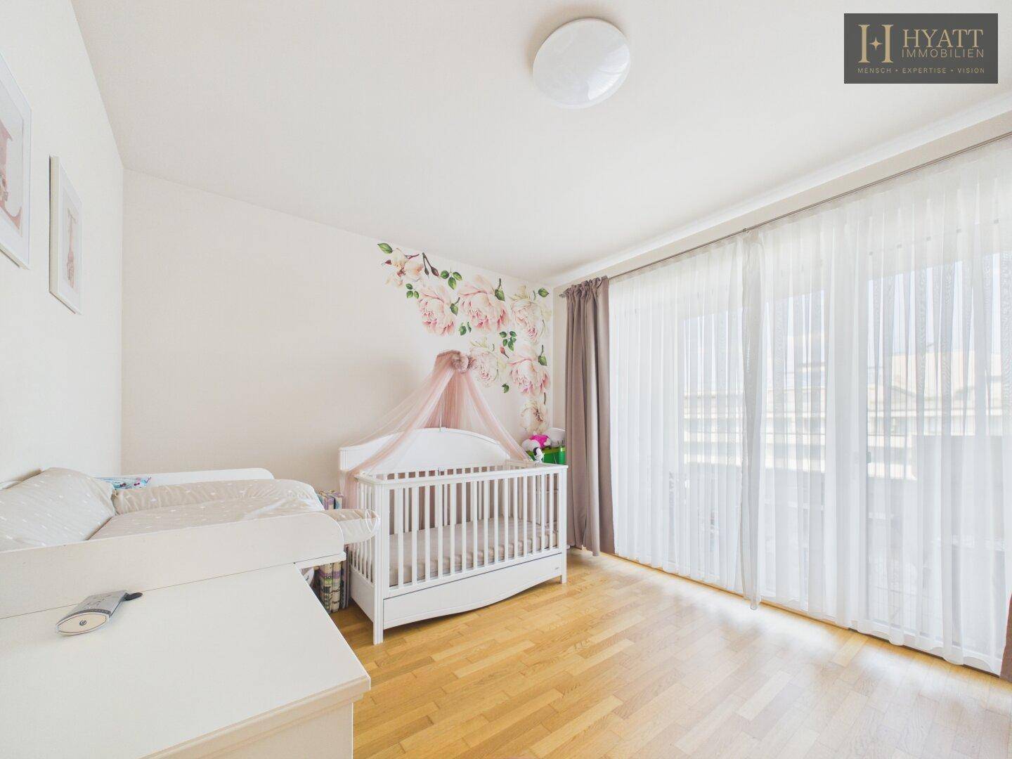 Helles Kinderzimmer mit Babybett, Wickeltisch und floraler Wanddekoration.