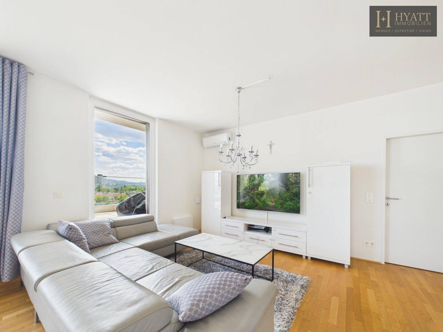 Helles Wohnzimmer mit modernem Sofa, Holzboden und Zugang zu großen Fenstern mit Aussicht.