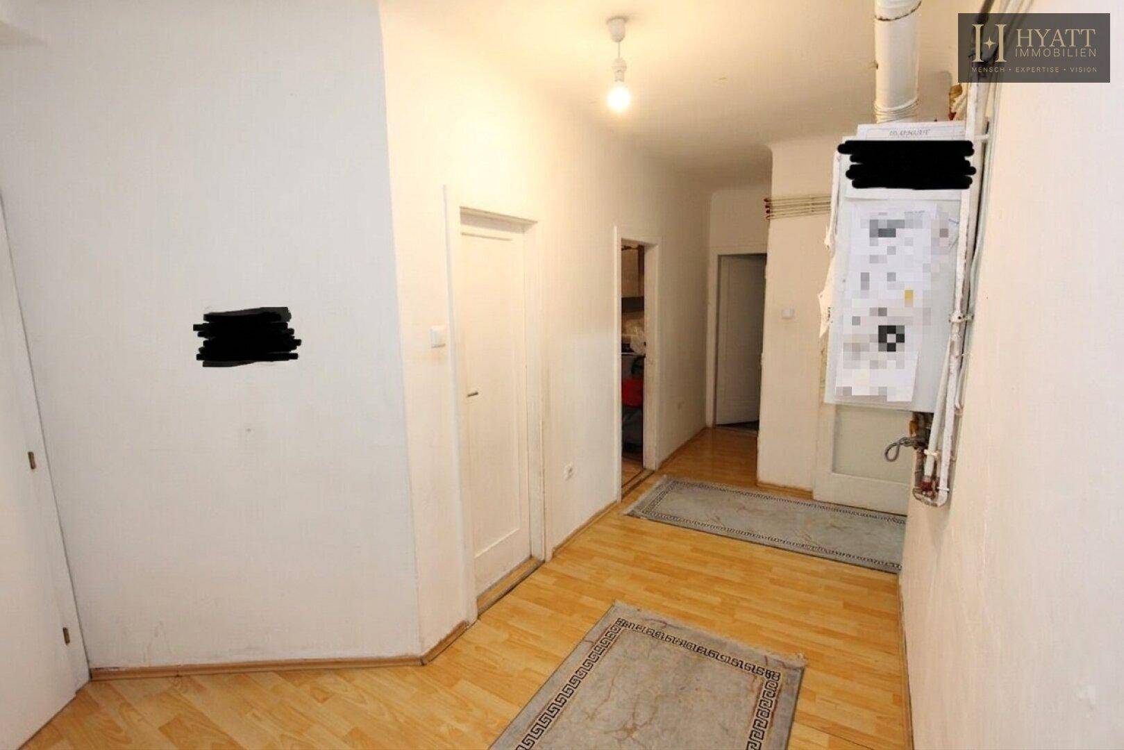 Heller Flur mit Holzboden und weißen Wänden, der zu weiteren Räumen führt.