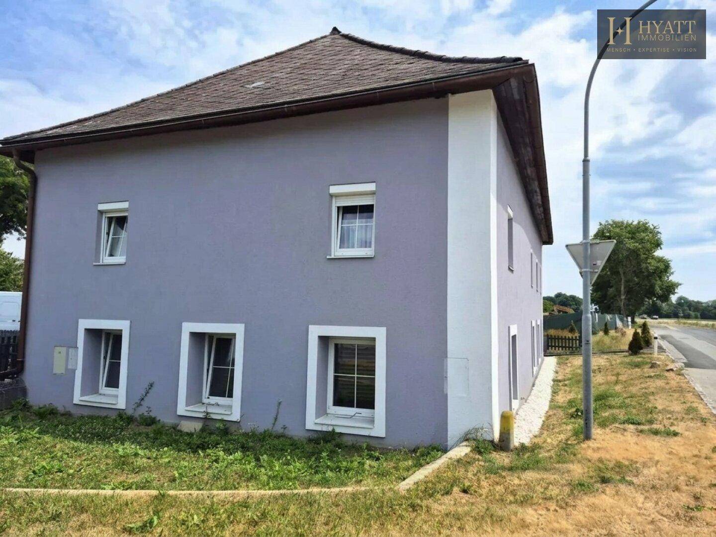 Seitenansicht des lila Gebäudes mit mehreren Fenstern und einer kleinen Rasenfläche daneben.