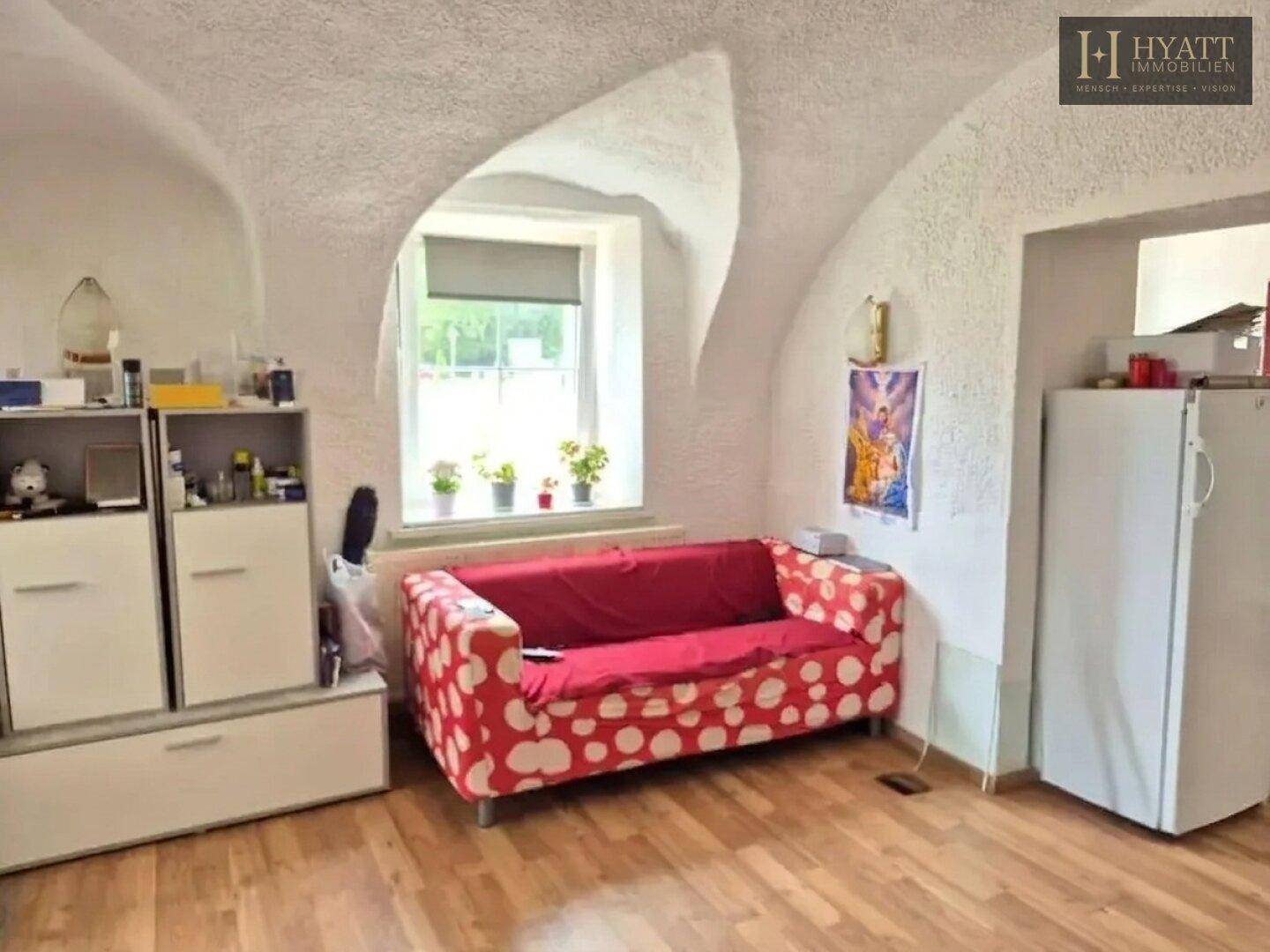Gemütliches Zimmer mit rotem Sofa, Holzboden und einzigartiger gewölbter Deckenstruktur.