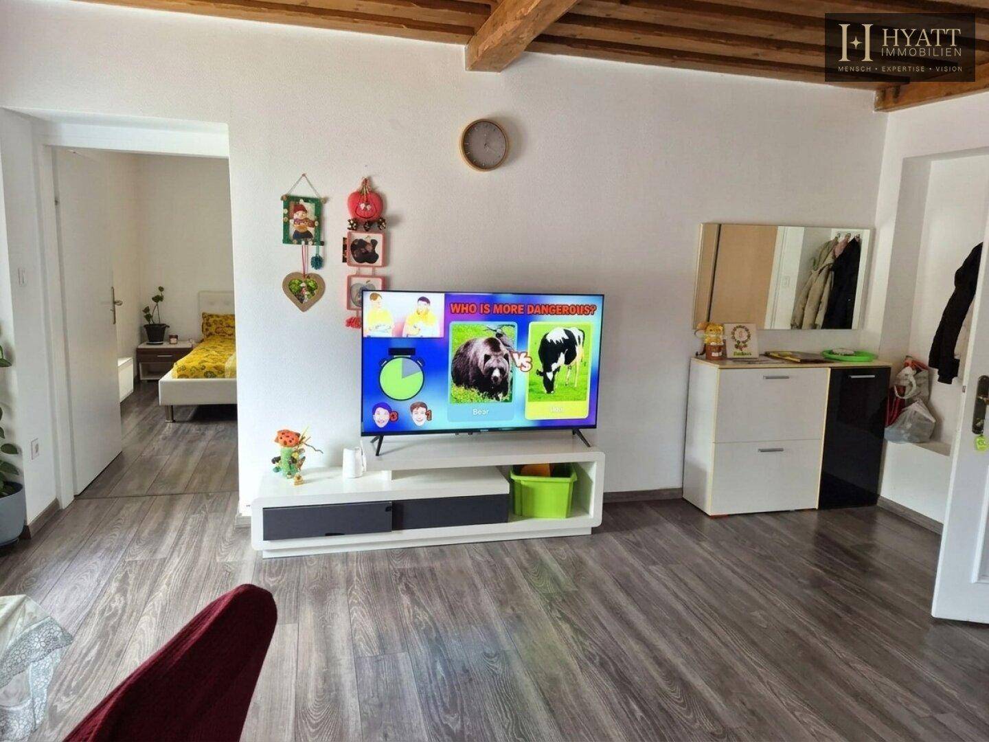 Wohnbereich mit Fernseher, Kommode und sichtbaren Holzbalken an der Decke.