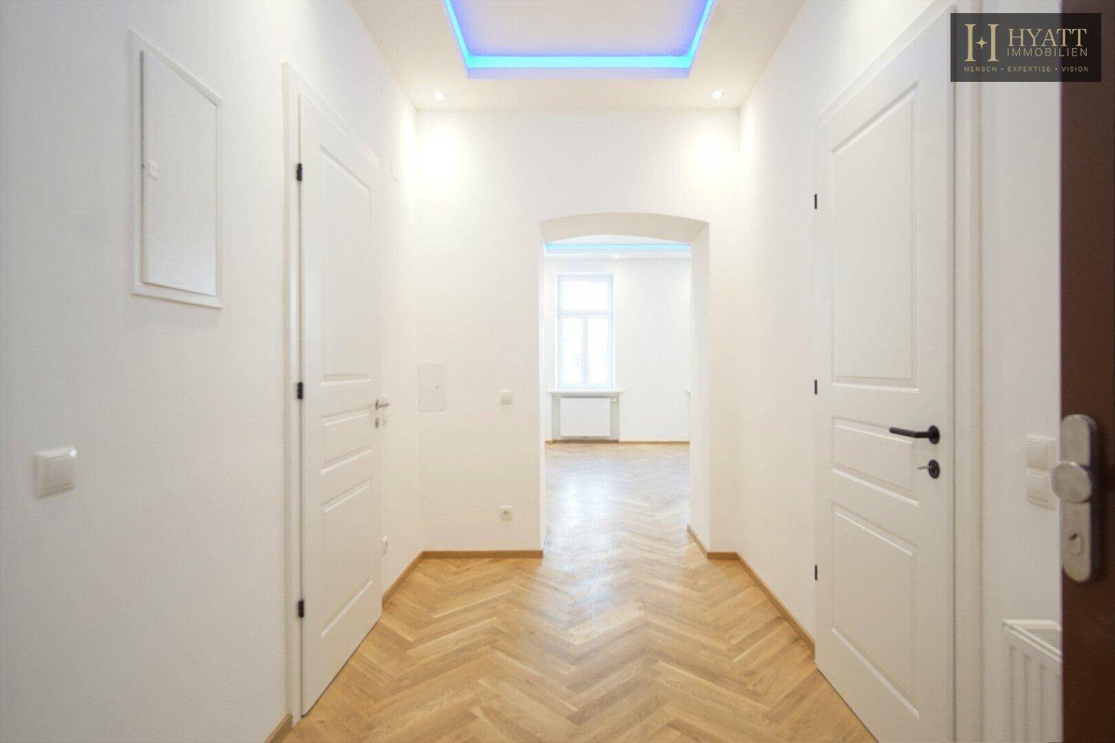 Heller Flur mit Fischgrätparkett, weißen Türen und moderner Deckenbeleuchtung.