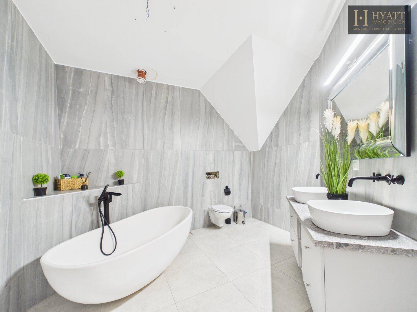 Modernes Badezimmer mit freistehender Badewanne, Doppelwaschbecken und grauen Fliesen.