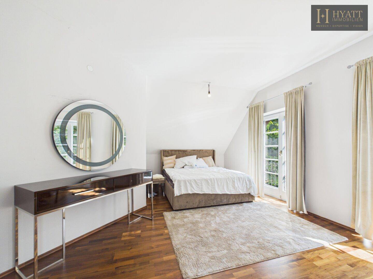 Helles Schlafzimmer mit Holzboden, großem Spiegel und Zugang zu einem Außenbereich.