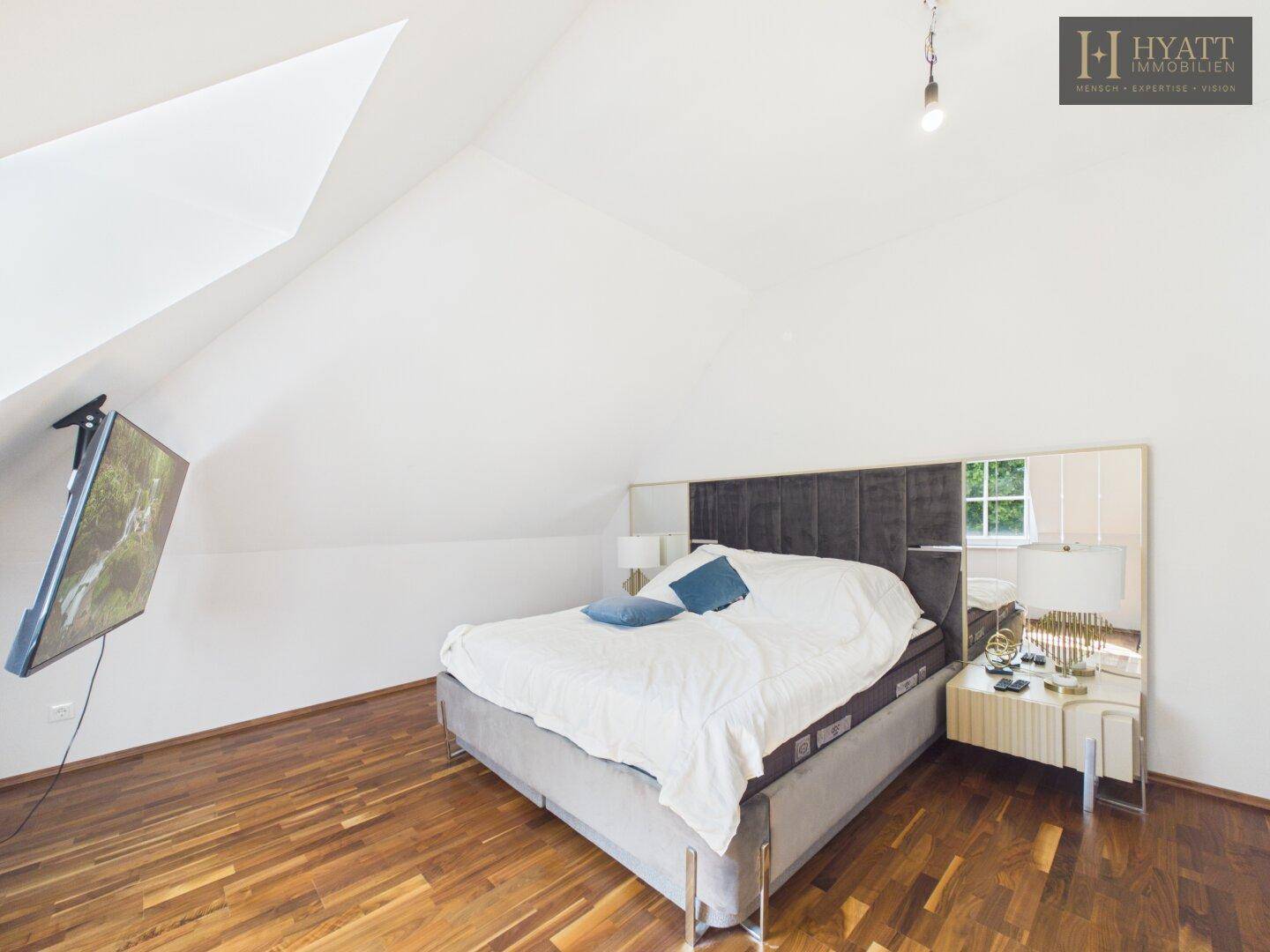 Gemütliches Schlafzimmer mit Holzboden, Dachschräge und Fernseher an der Wand.